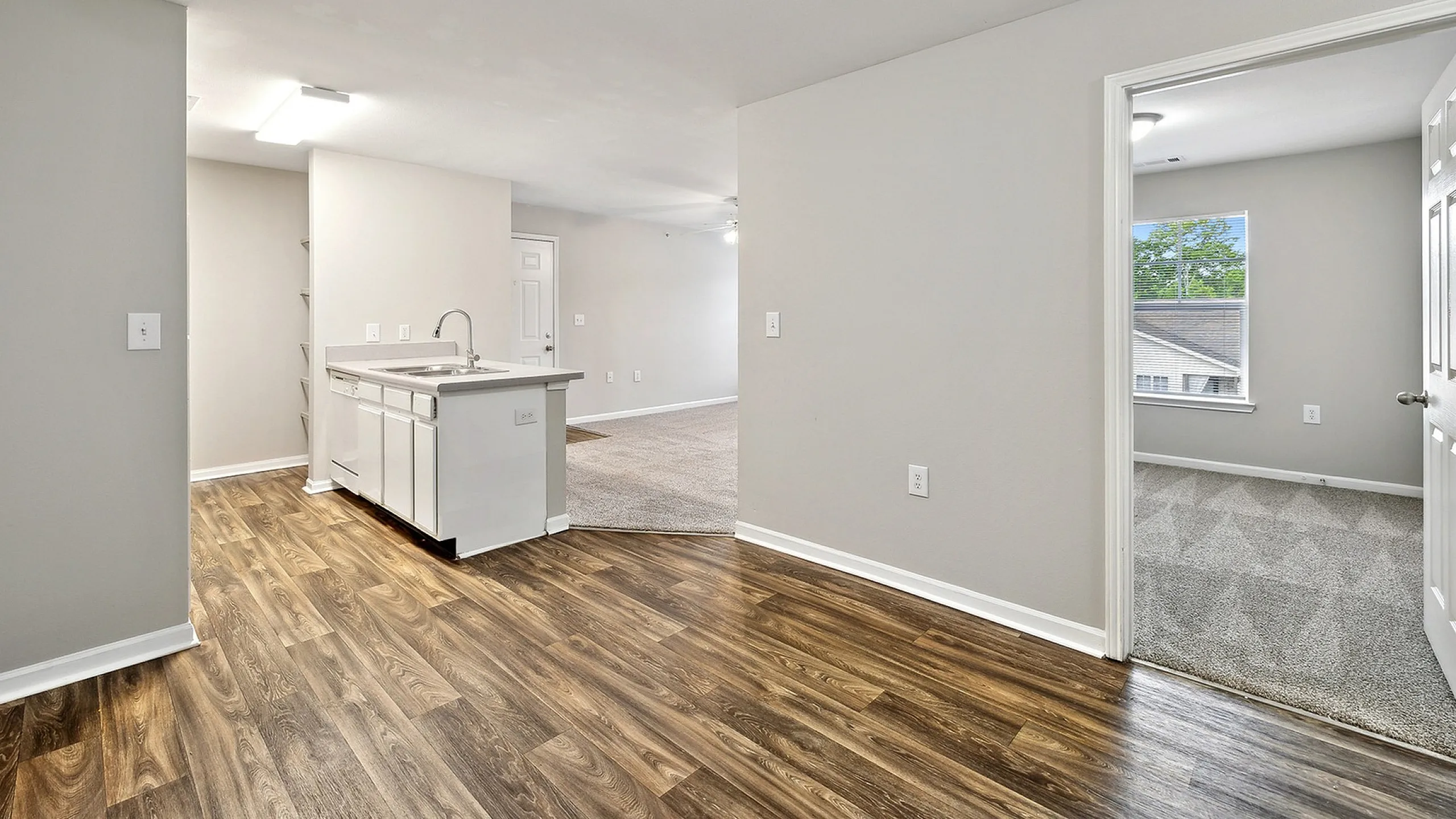 Contemporary apartment interior showcasing a modern kitchen with elegant wood flooring and a bright bedroom with plush carpet.