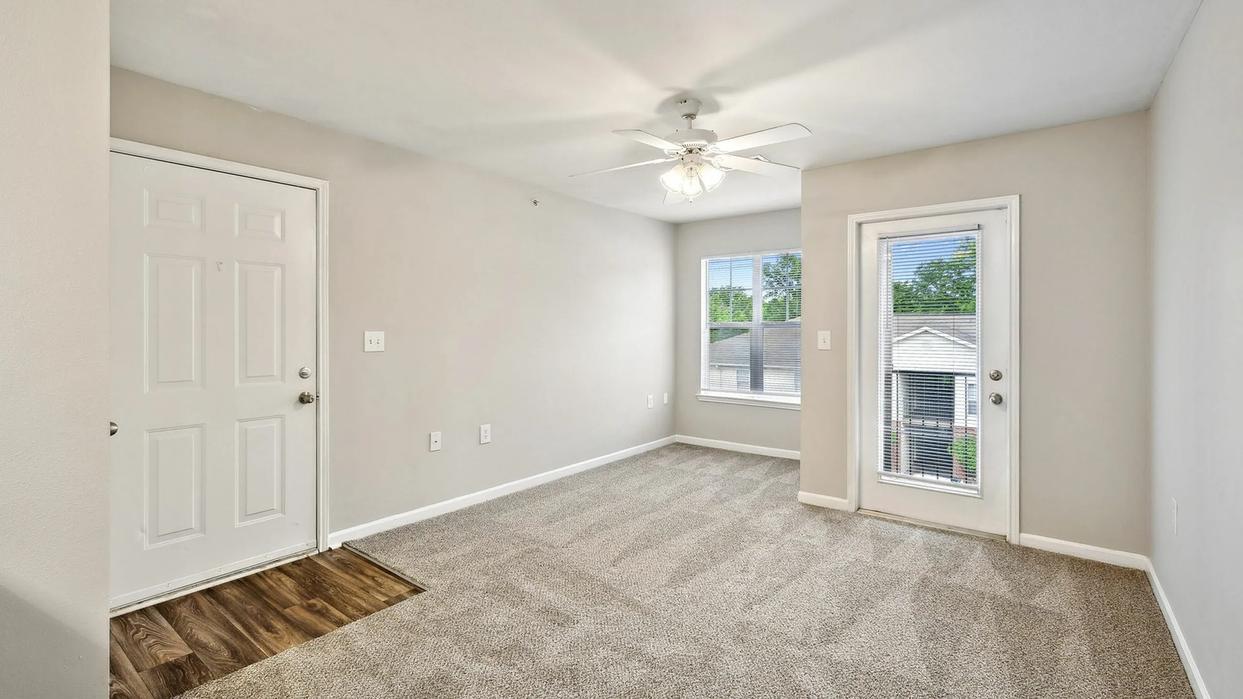 Bright and airy apartment room with plush carpeting, large window, and elegant ceiling fan, creating a welcoming atmosphere.