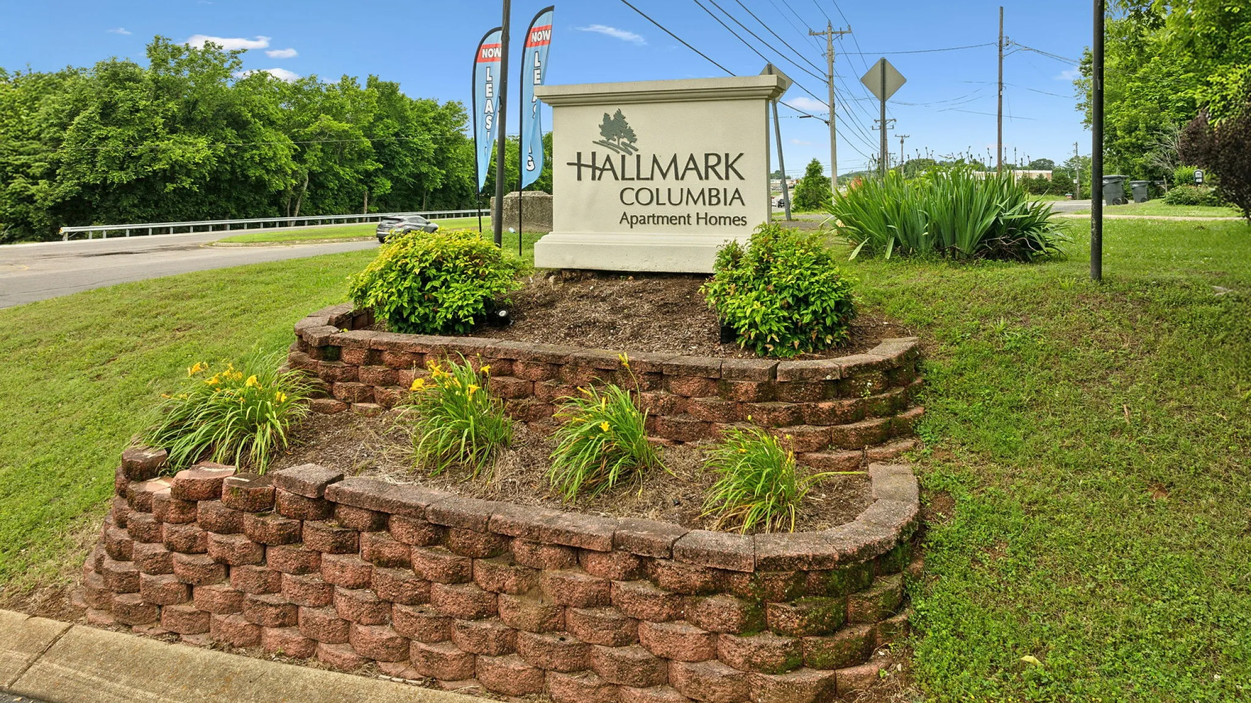 Inviting entrance to Hallmark Columbia Apartment Homes, showcasing lush landscaping and attractive brickwork on a sunny day.