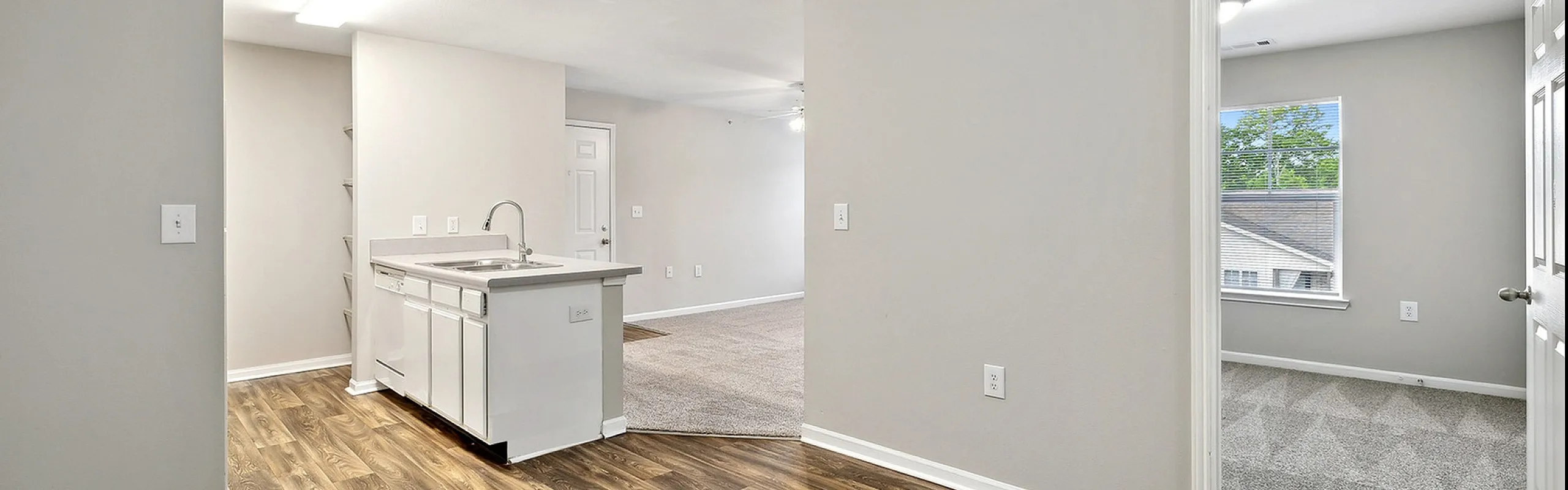 Contemporary open-floor apartment showcasing a sleek kitchen with stylish wood flooring, plush carpeted living area, and inviting natural light from large windows.