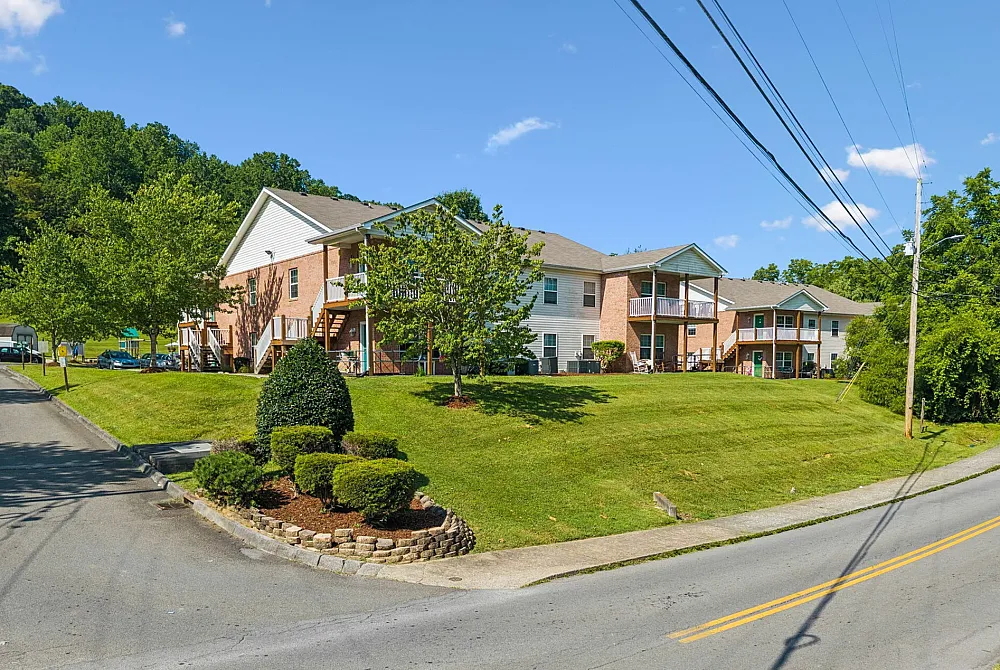 Charming suburban apartment complex with brick facade, lush green lawns, and scenic tree-lined surroundings.