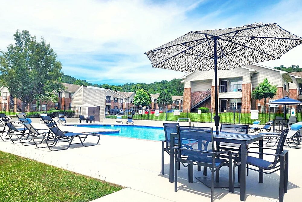 Inviting apartment community with a sparkling outdoor pool, elegant patio seating, and lush green surroundings under a clear blue sky.
