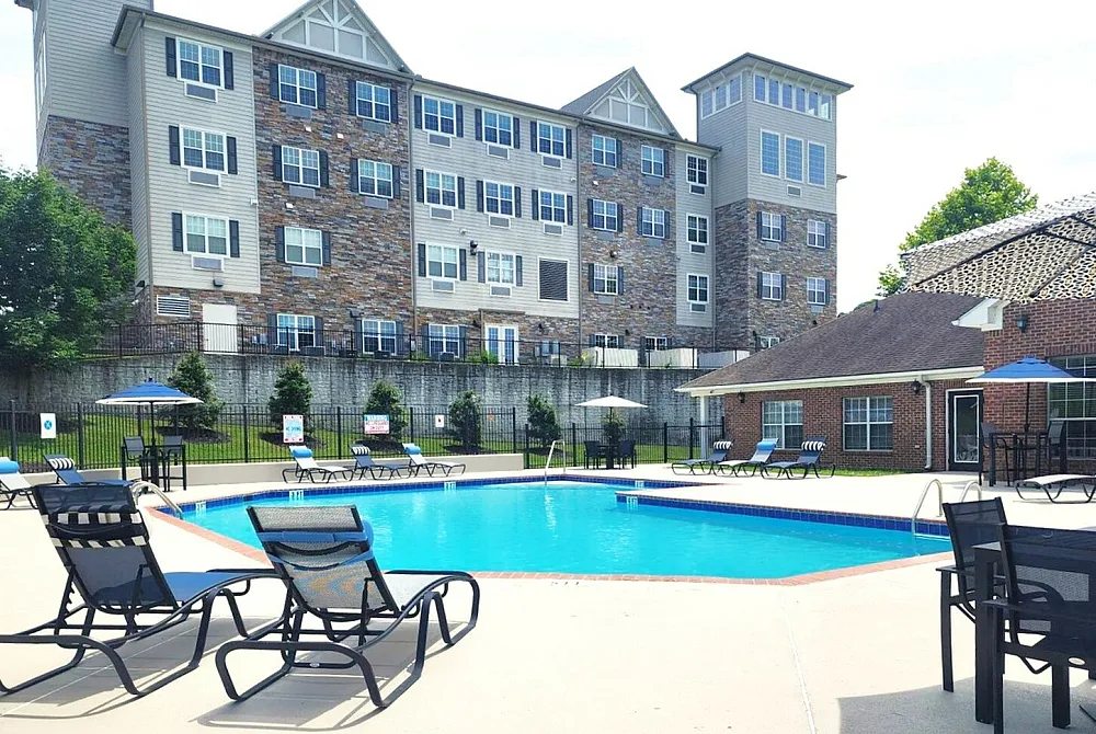 Inviting apartment complex with a sparkling outdoor swimming pool, surrounded by stylish lounge chairs and vibrant umbrellas, perfect for relaxation and leisure.