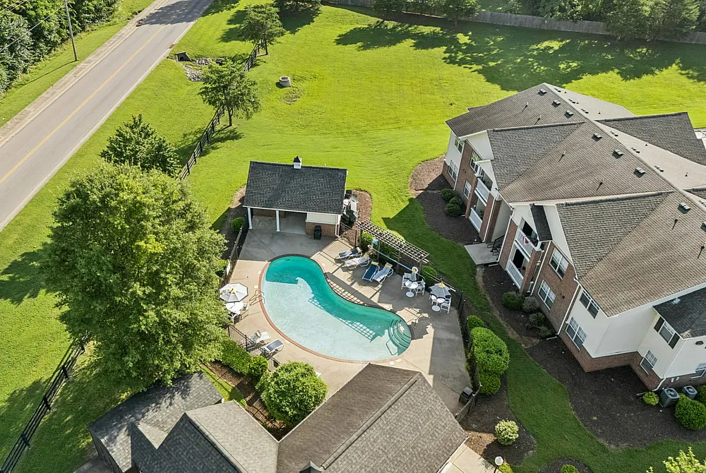 Inviting aerial view of charming apartment complex with a sparkling pool, lush green surroundings, and modern architecture.