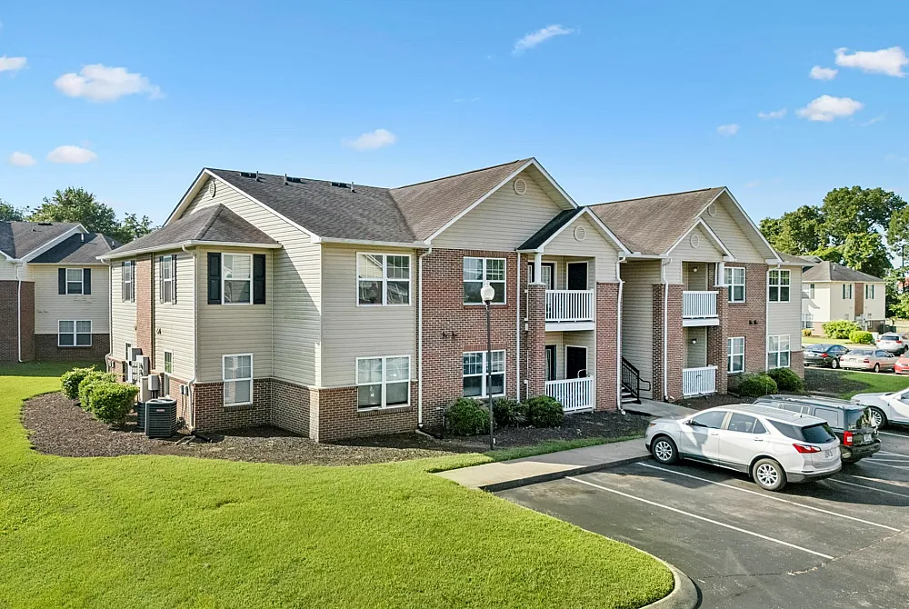 Charming suburban apartment building with brick accents, green lawns, and ample parking on a sunny day.