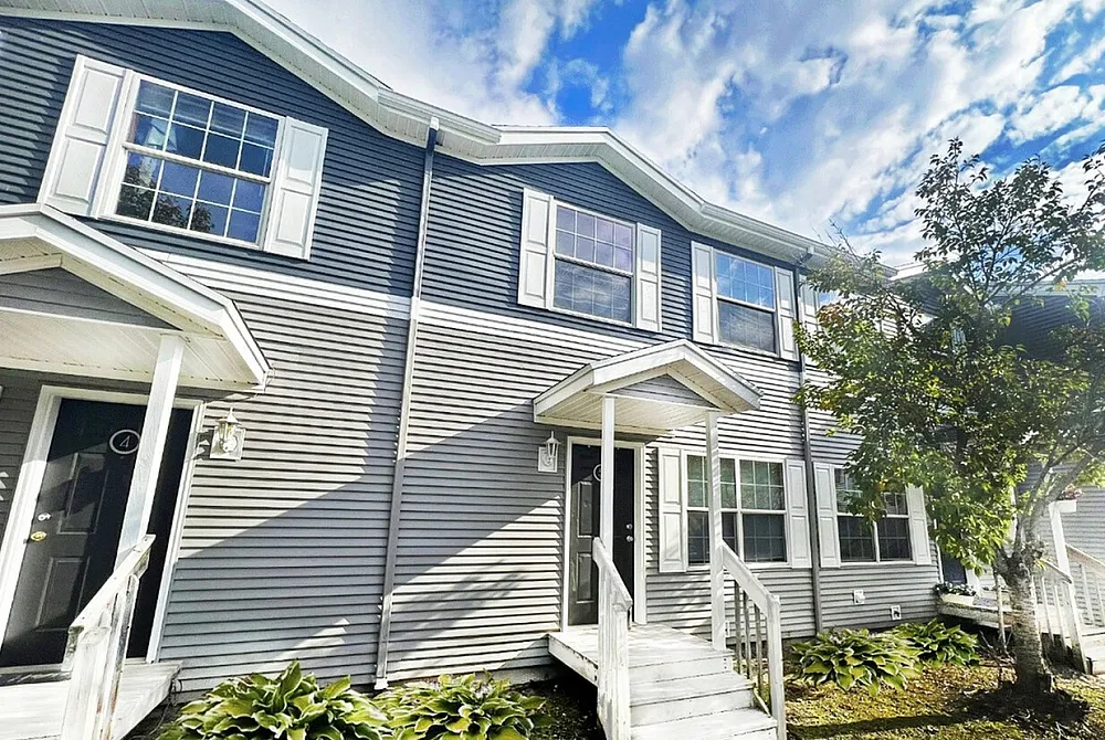Charming townhouse exterior with modern gray siding, inviting front porch, and vibrant landscaping under a bright blue sky.