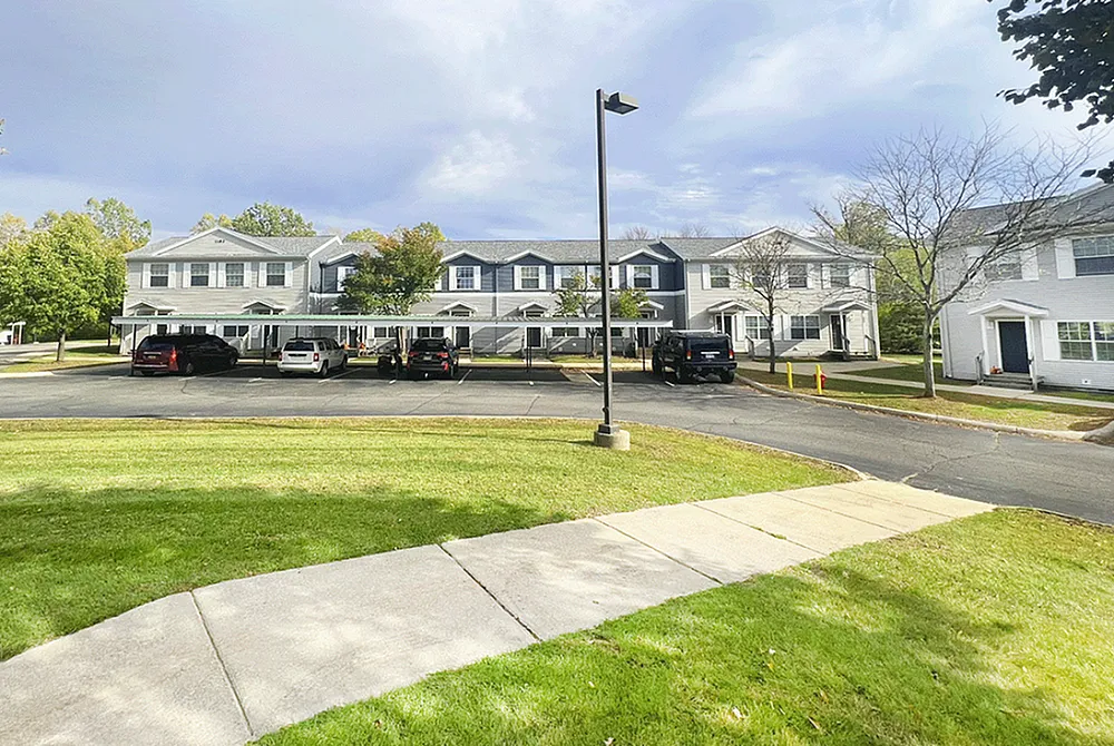 Charming row of townhouses with a bright exterior, ample parking, and lush green surroundings under a serene sky.