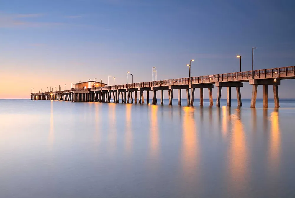 Mesmerizing sunset view of a beautifully lit pier extending into tranquil waters, offering a serene and picturesque coastal experience.