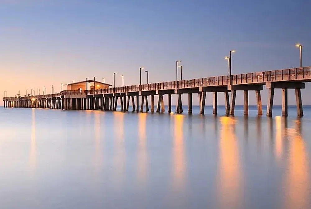 Serene pier extending over tranquil waters at dusk, with soft reflections and a warm, inviting glow.