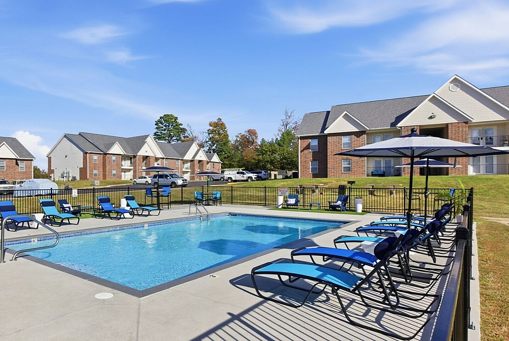 Inviting outdoor pool area with sleek loungers and sun umbrellas, surrounded by charming brick apartment buildings under a bright blue sky.