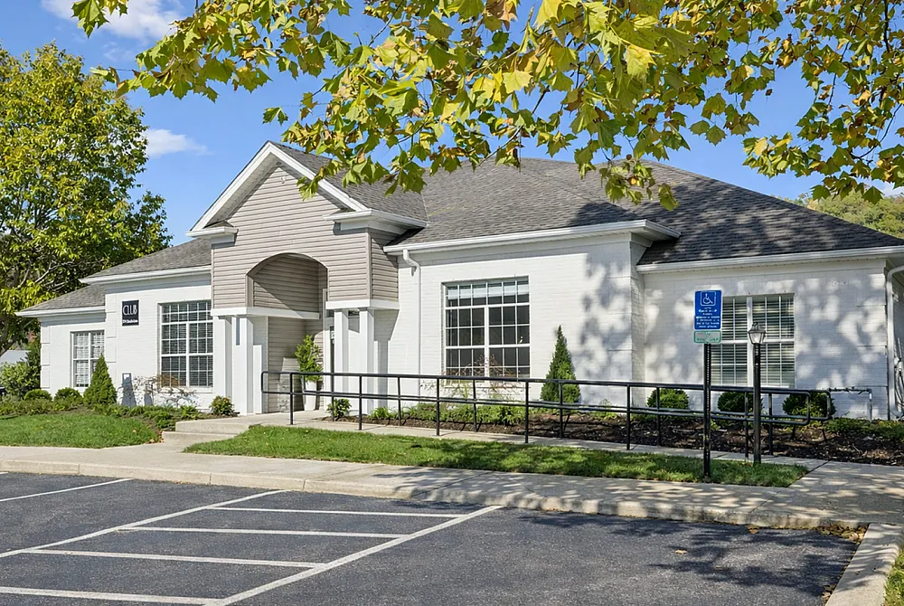 Charming clubhouse exterior with classic design, lush green landscaping, and inviting entryway under a clear blue sky.