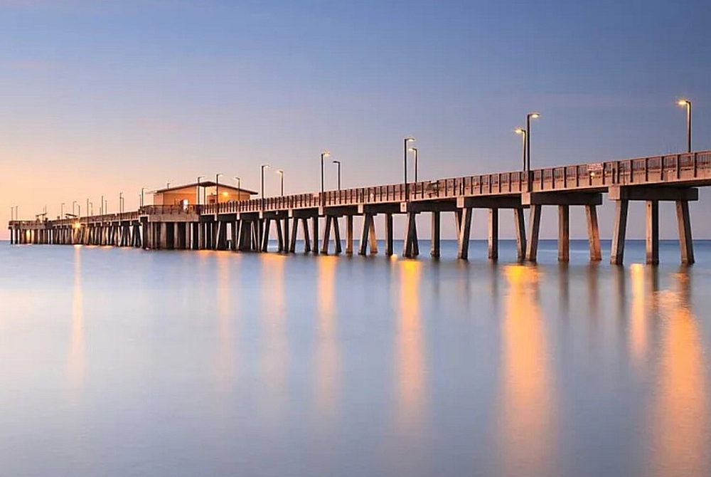 Scenic view of a tranquil pier extending over calm waters at sunset, reflecting ambient lights.