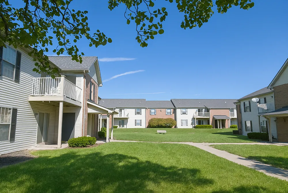 Charming apartment complex with manicured lawns, leafy trees, and inviting balconies under a clear blue sky.
