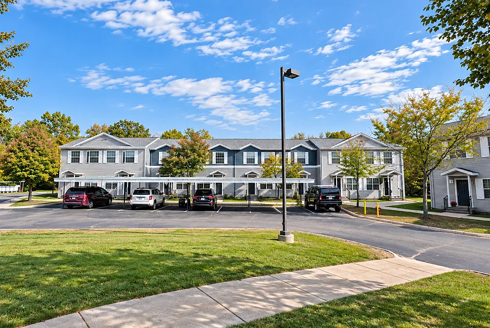 Charming townhouse community with lush greenery, ample parking, and modern architecture under a bright blue sky.