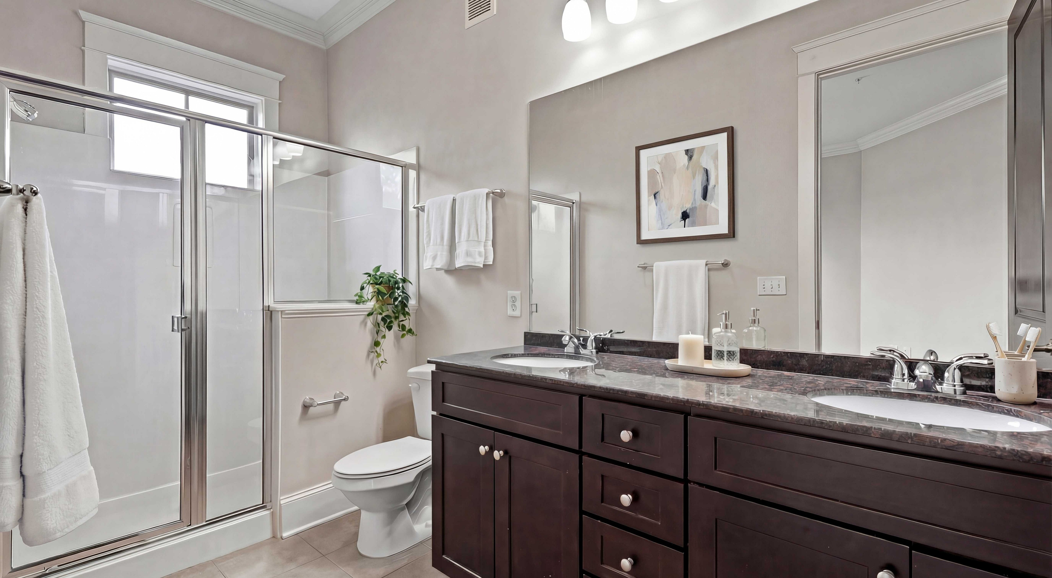 Modern bathroom with sleek dark wood cabinetry, elegant double sinks, and a spacious glass-enclosed shower, accented by stylish decor and natural light.