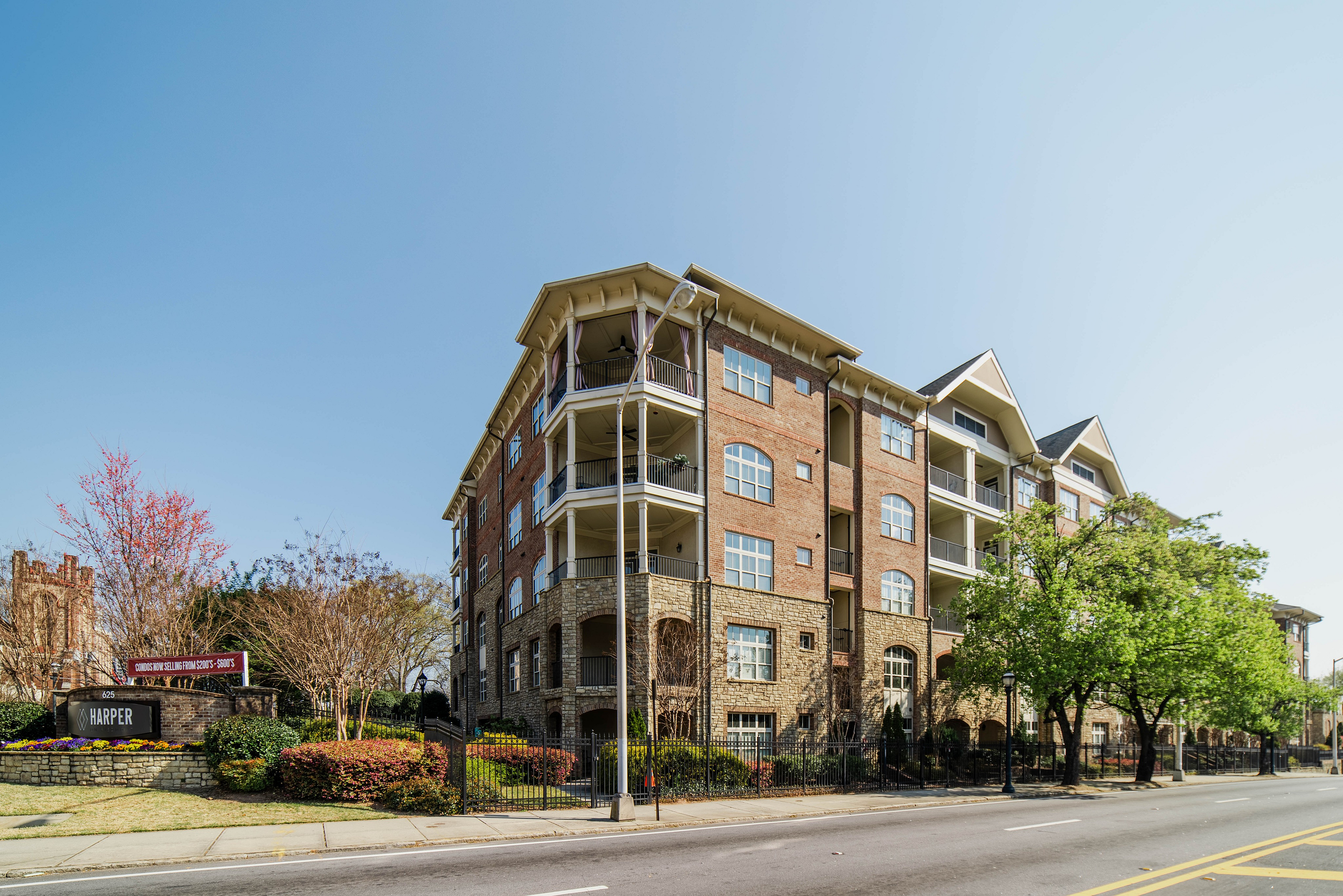 Charming brick apartment building with elegant balconies and lush landscaping, situated on a vibrant city street under a clear blue sky.