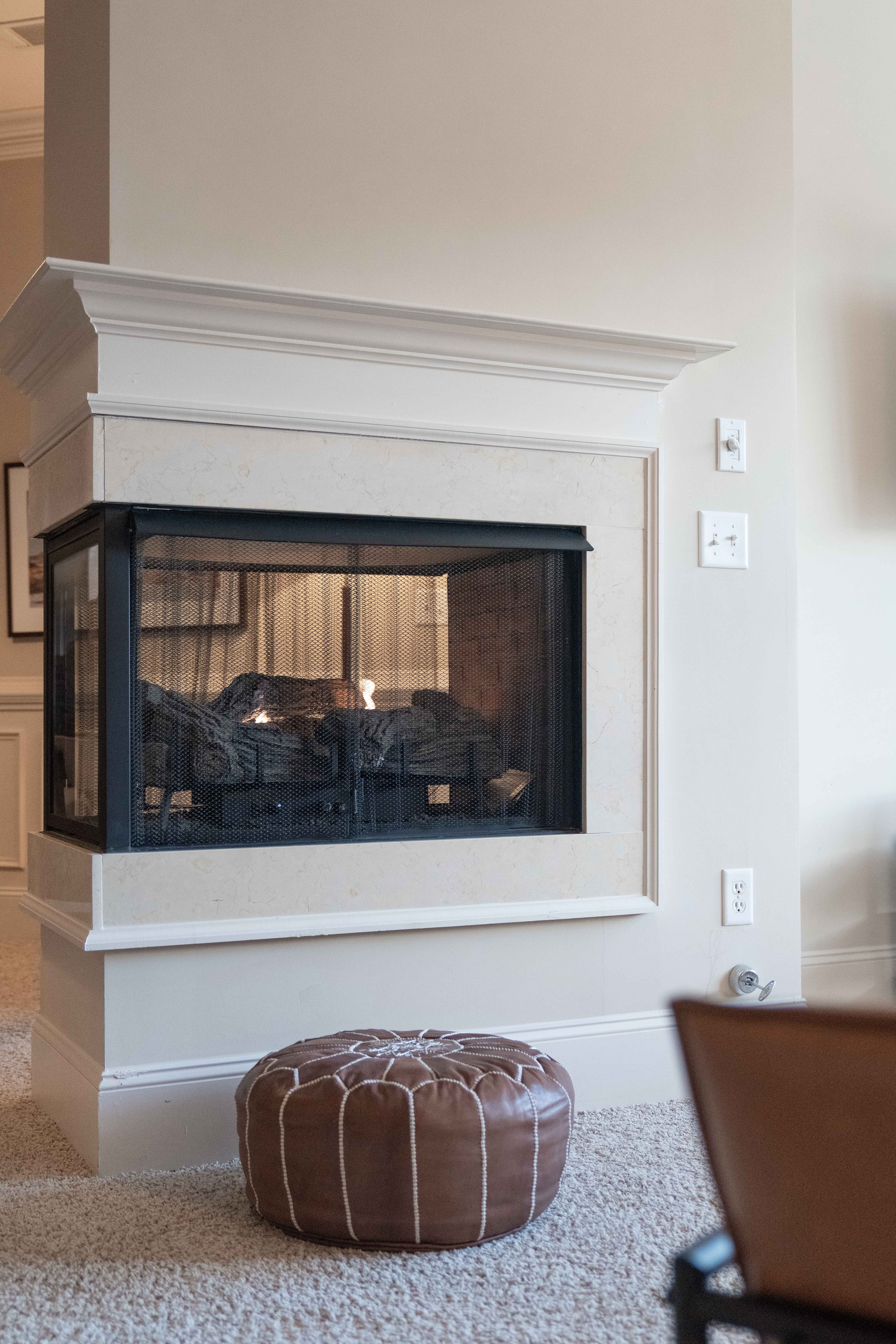 Inviting living area featuring a modern fireplace with a chic brown pouf, promising warmth and comfort.