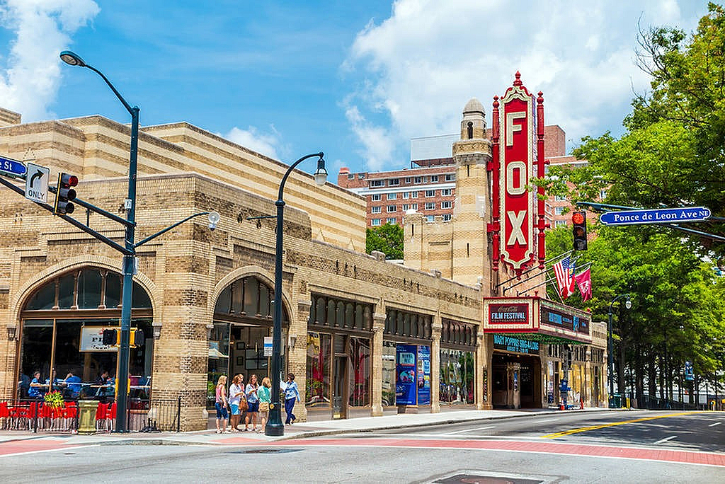 Vibrant street view of historic architecture with iconic marquee, bustling with pedestrians under a clear blue sky.