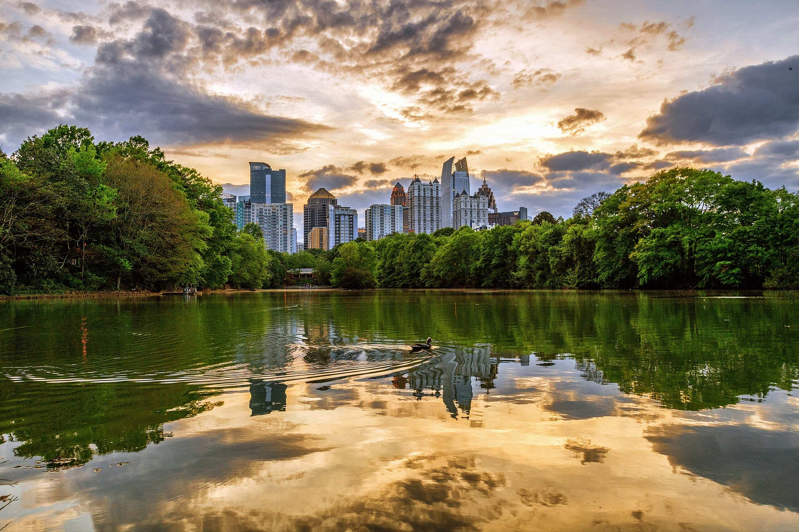 Captivating city skyline reflecting on a tranquil lake at sunset, surrounded by lush greenery.