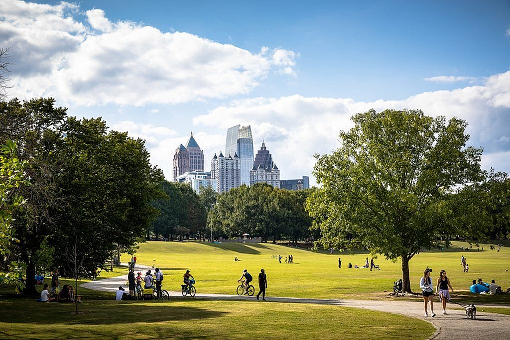 Vibrant city park scene with lush greenery, people enjoying outdoor activities, and a stunning skyline backdrop.