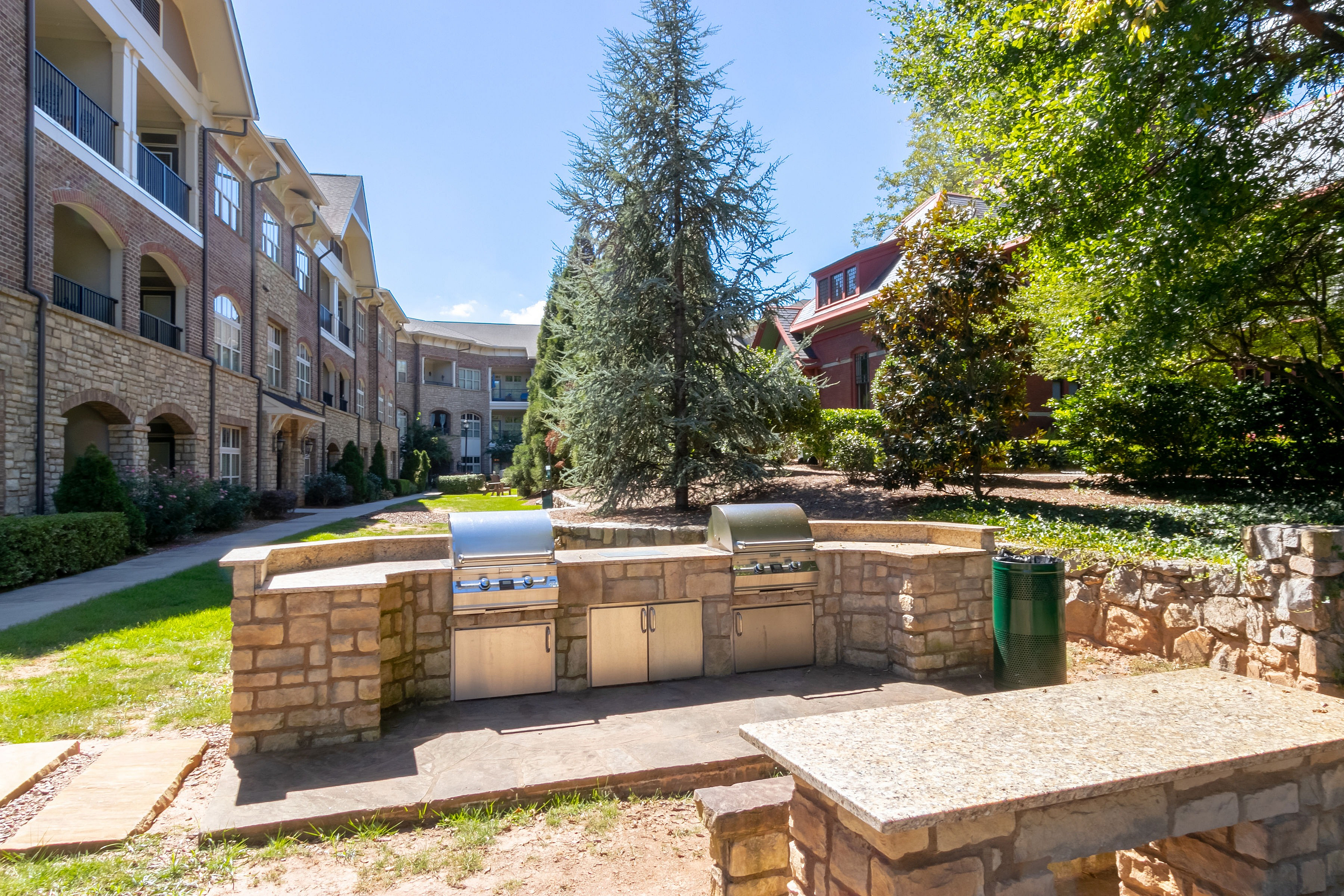 Charming apartment courtyard featuring elegant stone architecture and a modern outdoor grill area surrounded by lush greenery and scenic views.
