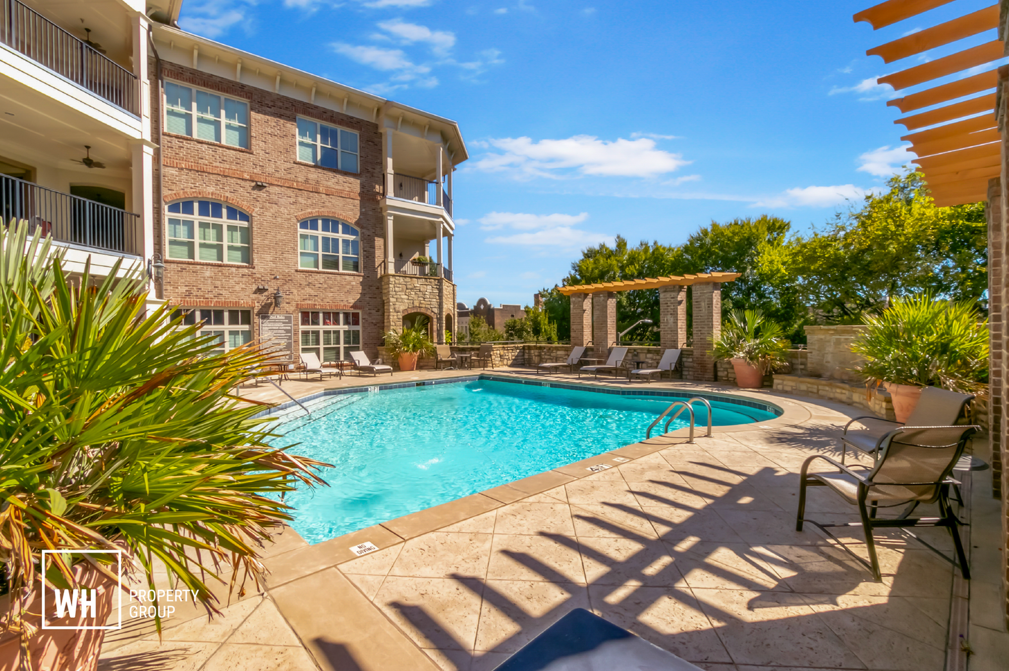 Luxurious outdoor pool area with elegant lounge chairs and lush greenery, perfect for relaxation under the clear blue sky.