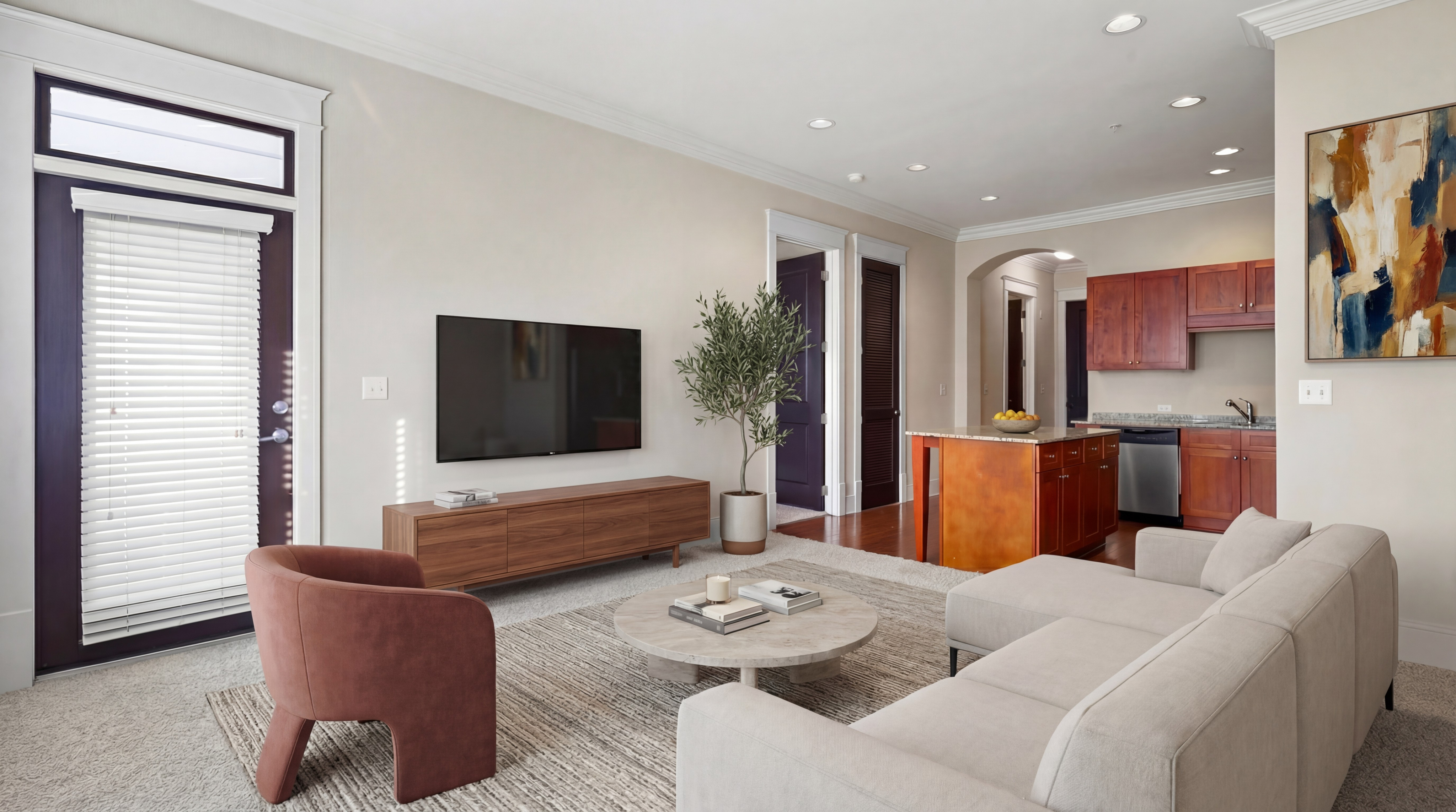 Modern open-concept living room featuring a cozy sofa, chic accent chair, and elegant wooden cabinetry leading to a stylish kitchen with updated appliances.