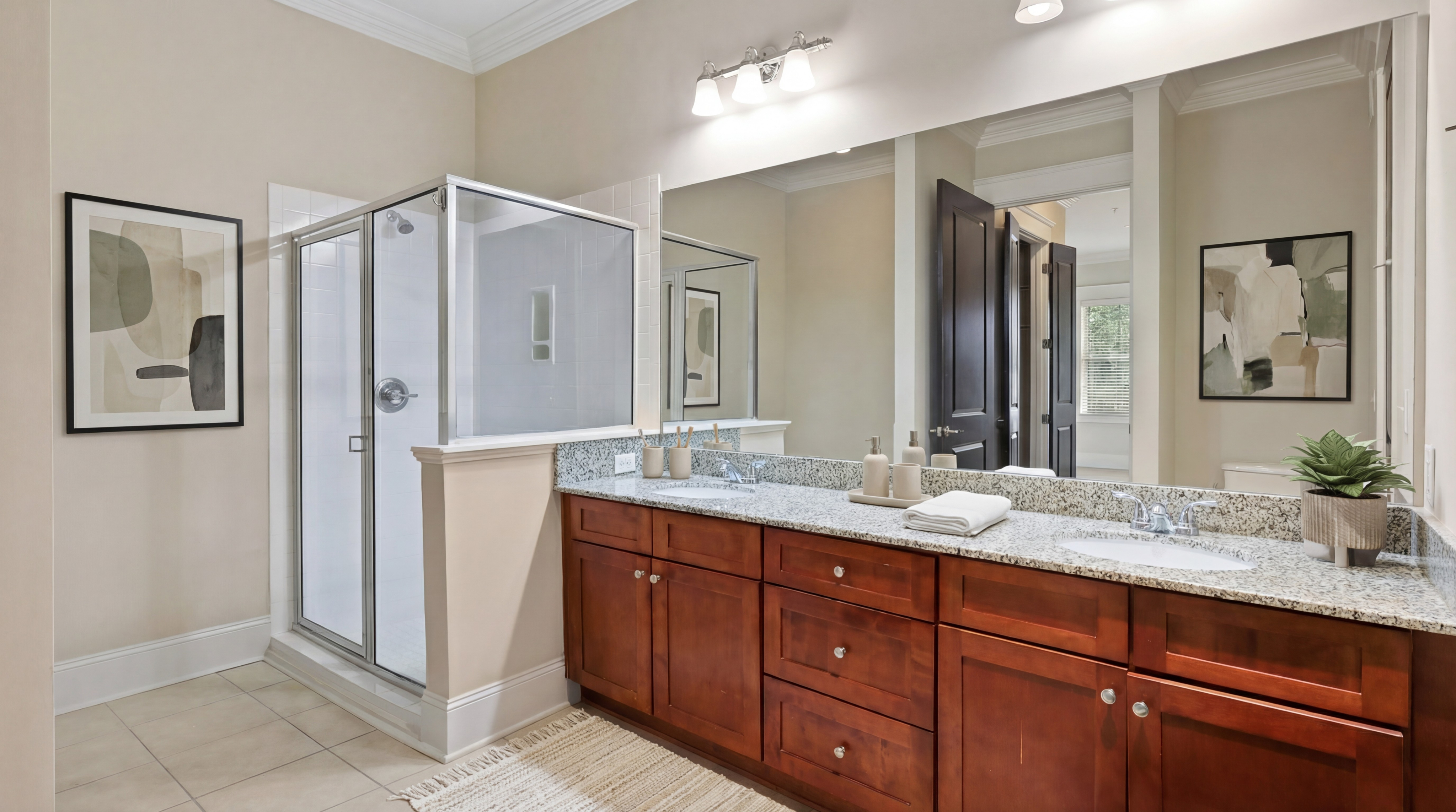 Elegant bathroom showcasing a granite countertop with dual sinks, stylish wood cabinetry, glass-enclosed shower, and modern decor accents.