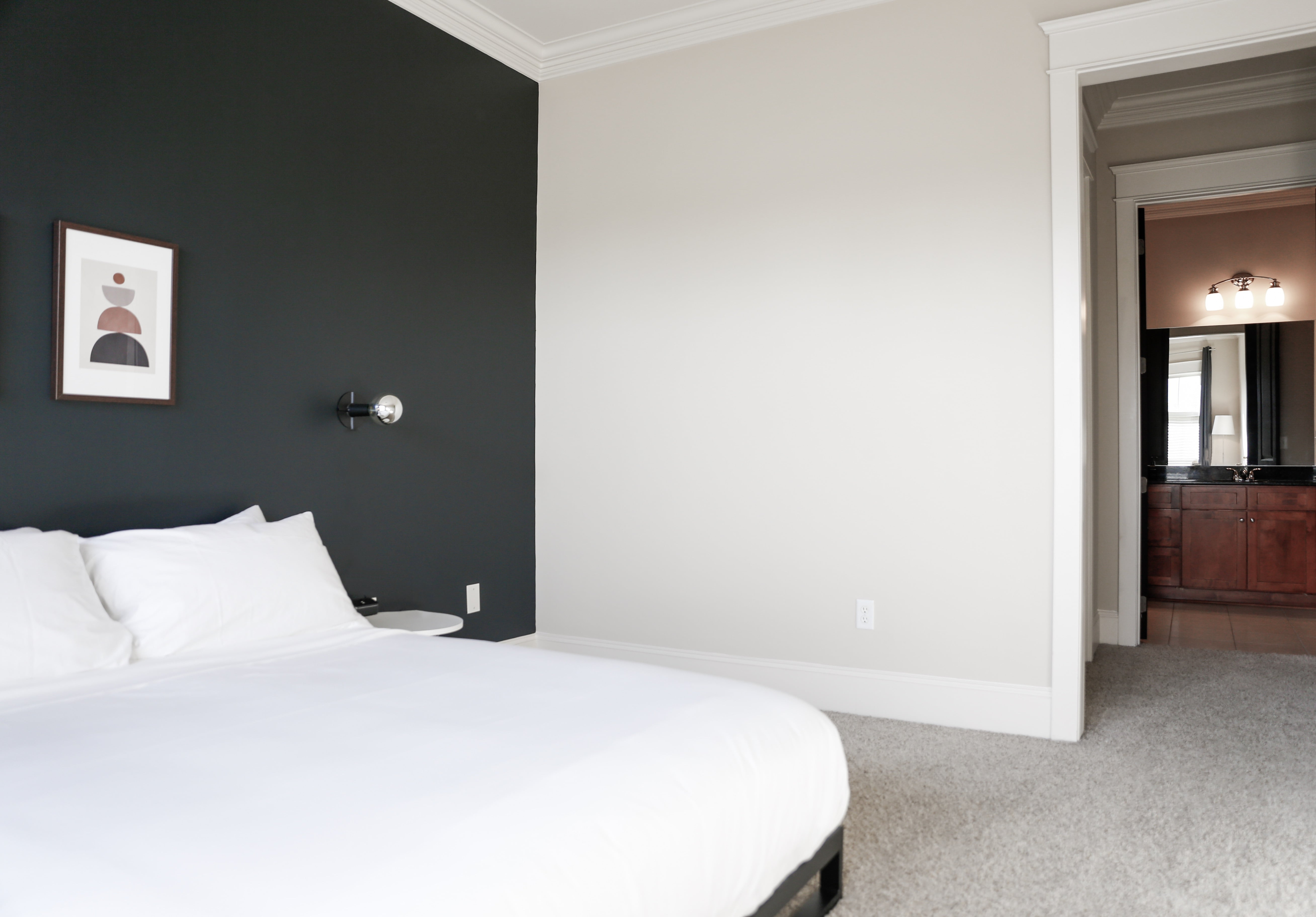 Modern minimalist bedroom with a cozy atmosphere, featuring a dark accent wall, elegant wall art, and a glimpse of a stylish bathroom.