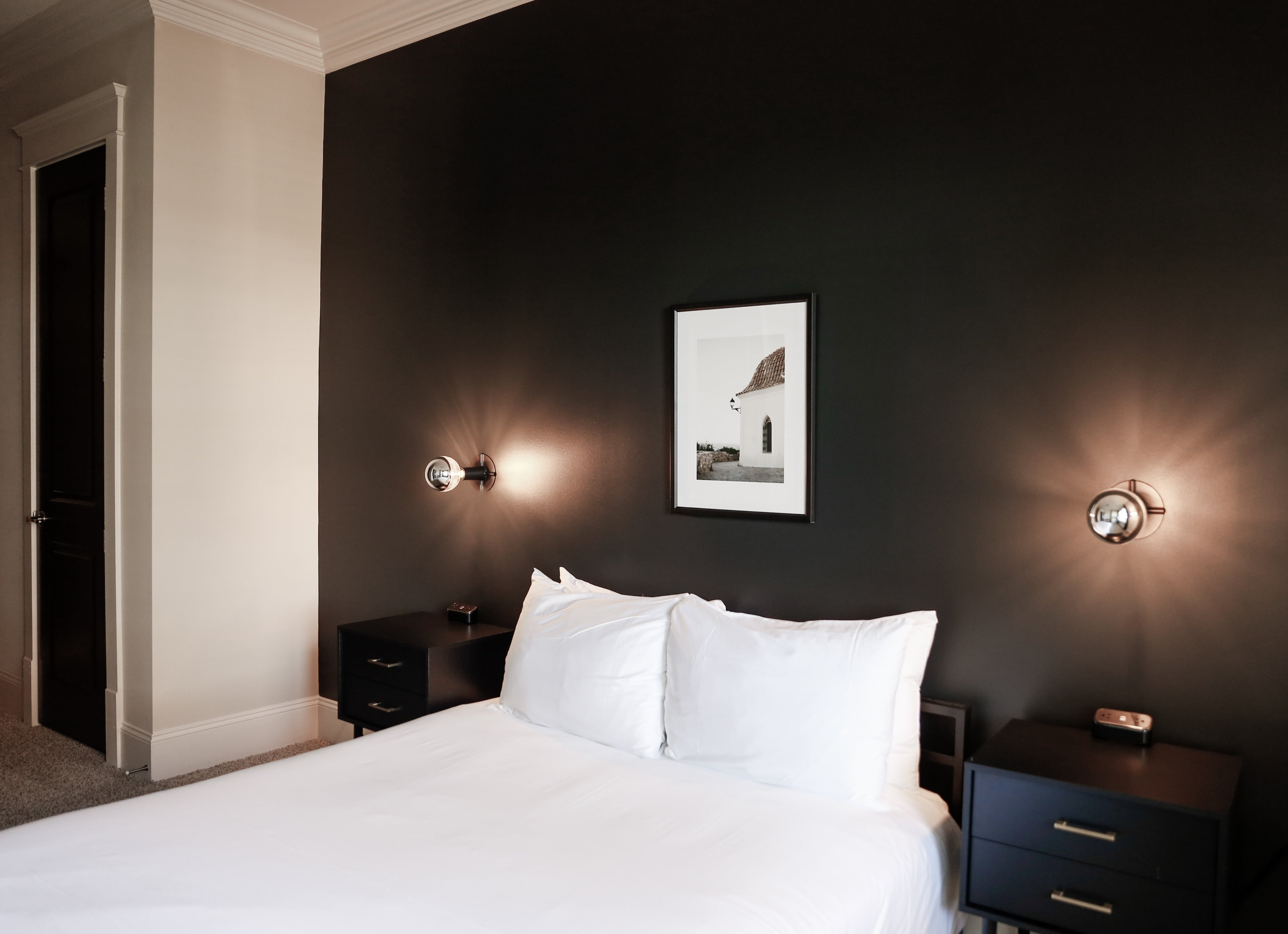 Elegant bedroom with modern black feature wall, cozy white bed, stylish bedside tables, and chic lighting.