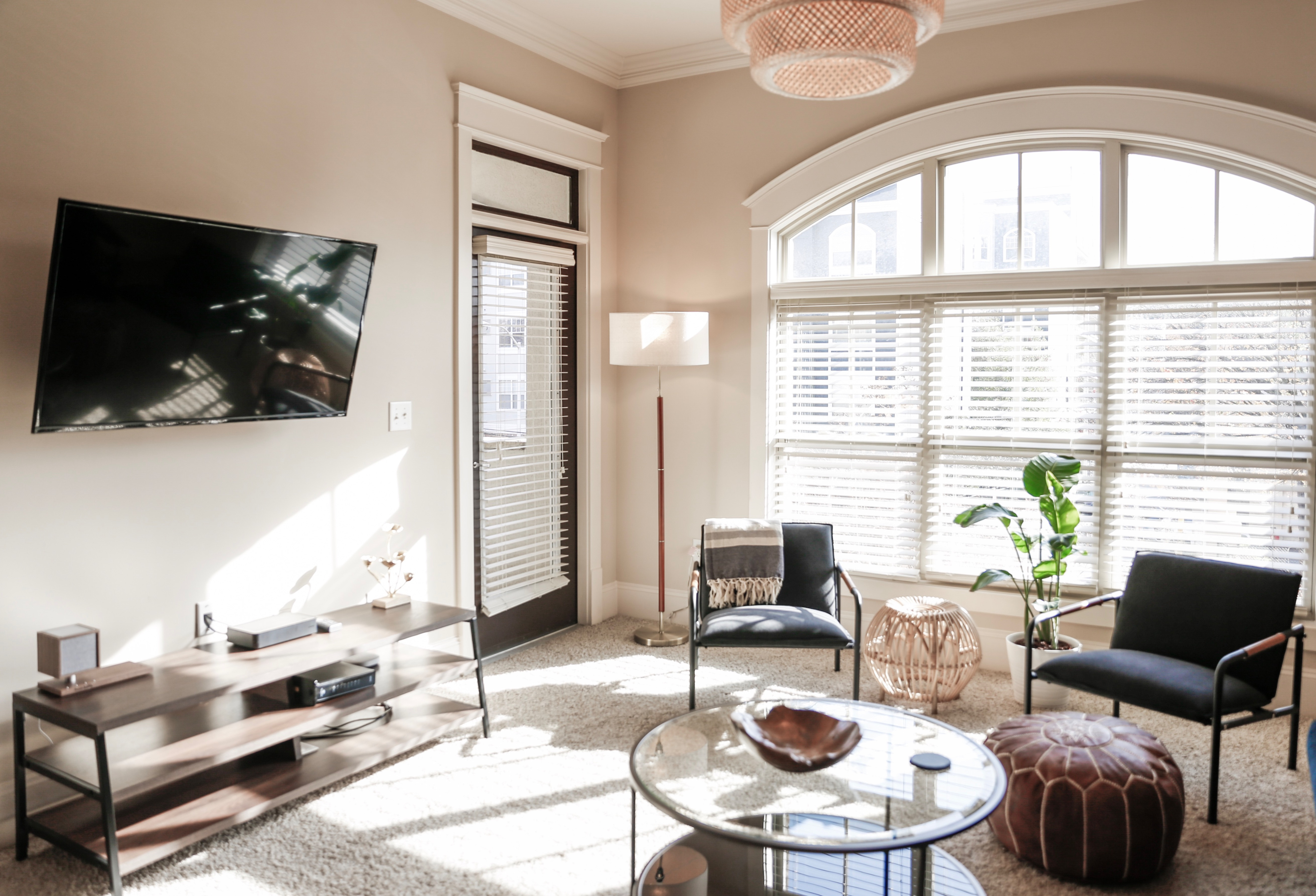 Bright and inviting living room with modern decor, featuring a wall-mounted TV, stylish furniture, and large arched windows allowing ample natural light.