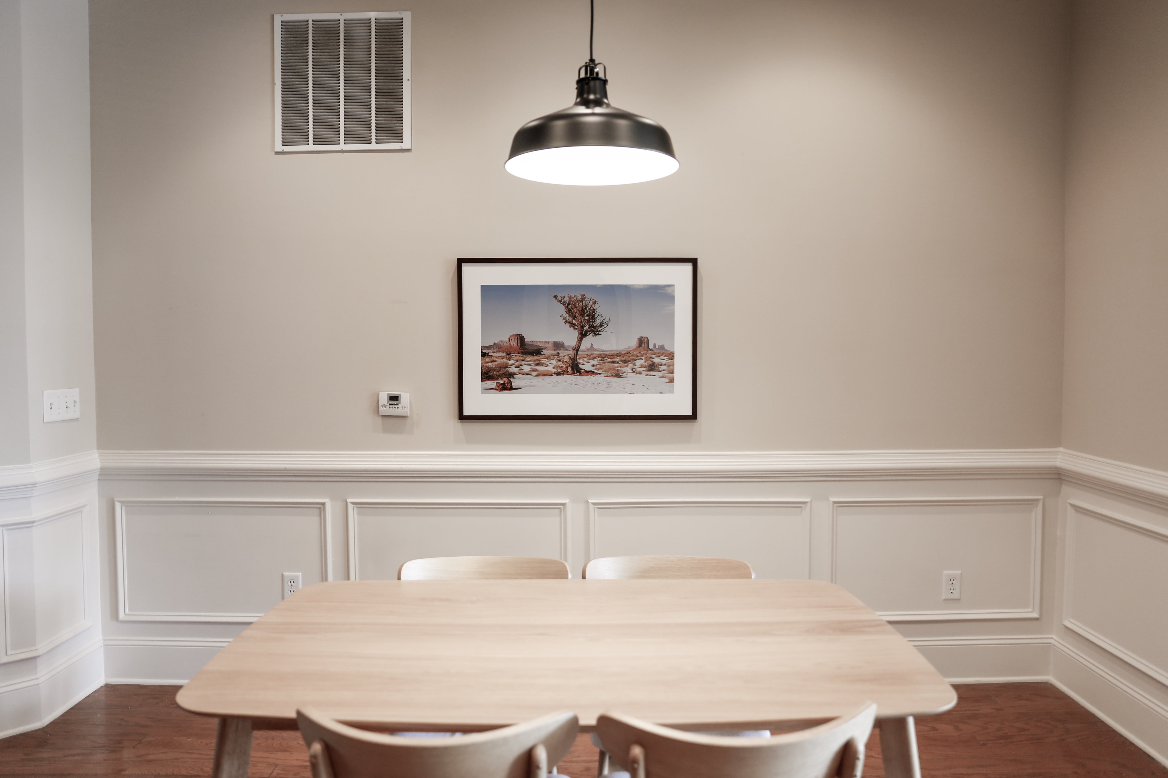 Bright dining area highlighted by a stylish wooden table and modern lighting, featuring chic wainscoting and a captivating desert landscape artwork.