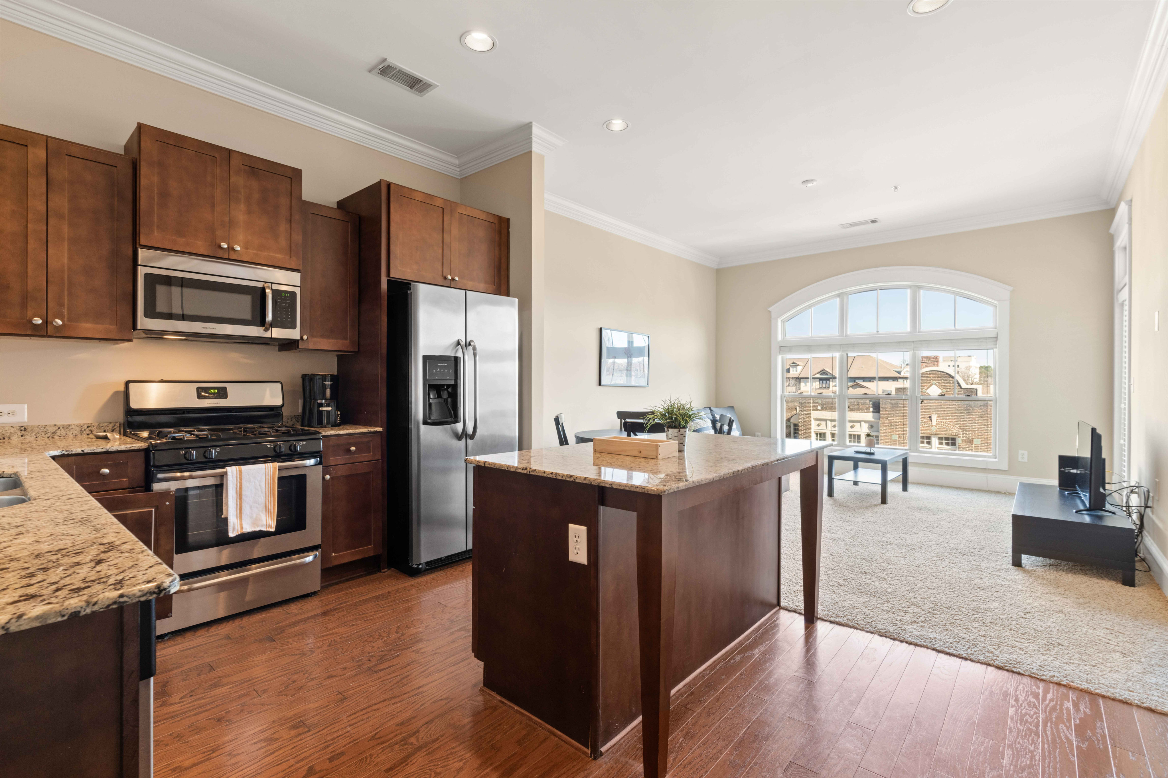 Elegant open-concept kitchen and living area with granite countertops, stainless steel appliances, and large arched window providing natural light.