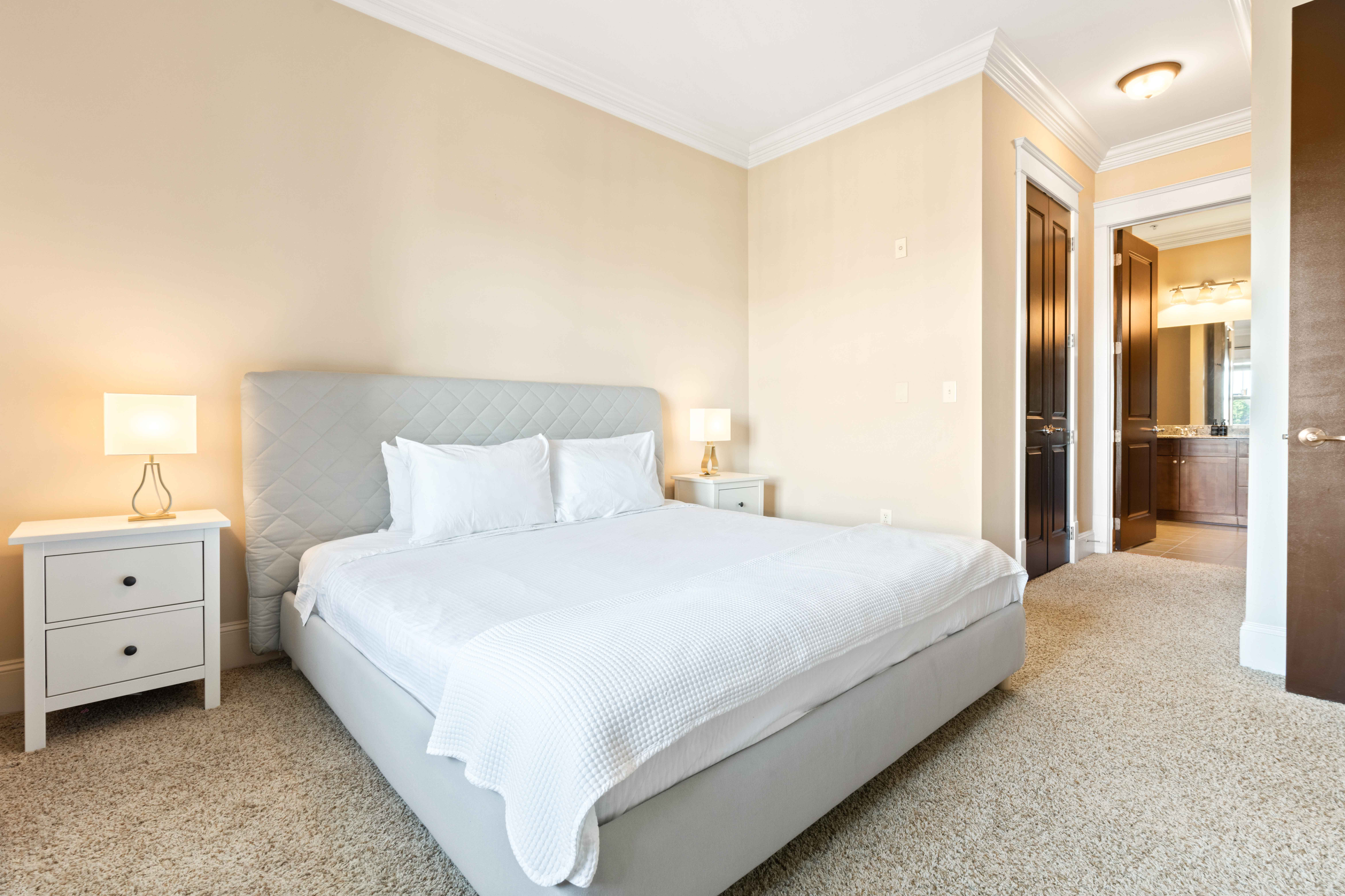 Bright and elegant bedroom with plush carpet, a cozy king-sized bed, and modern en-suite bathroom.