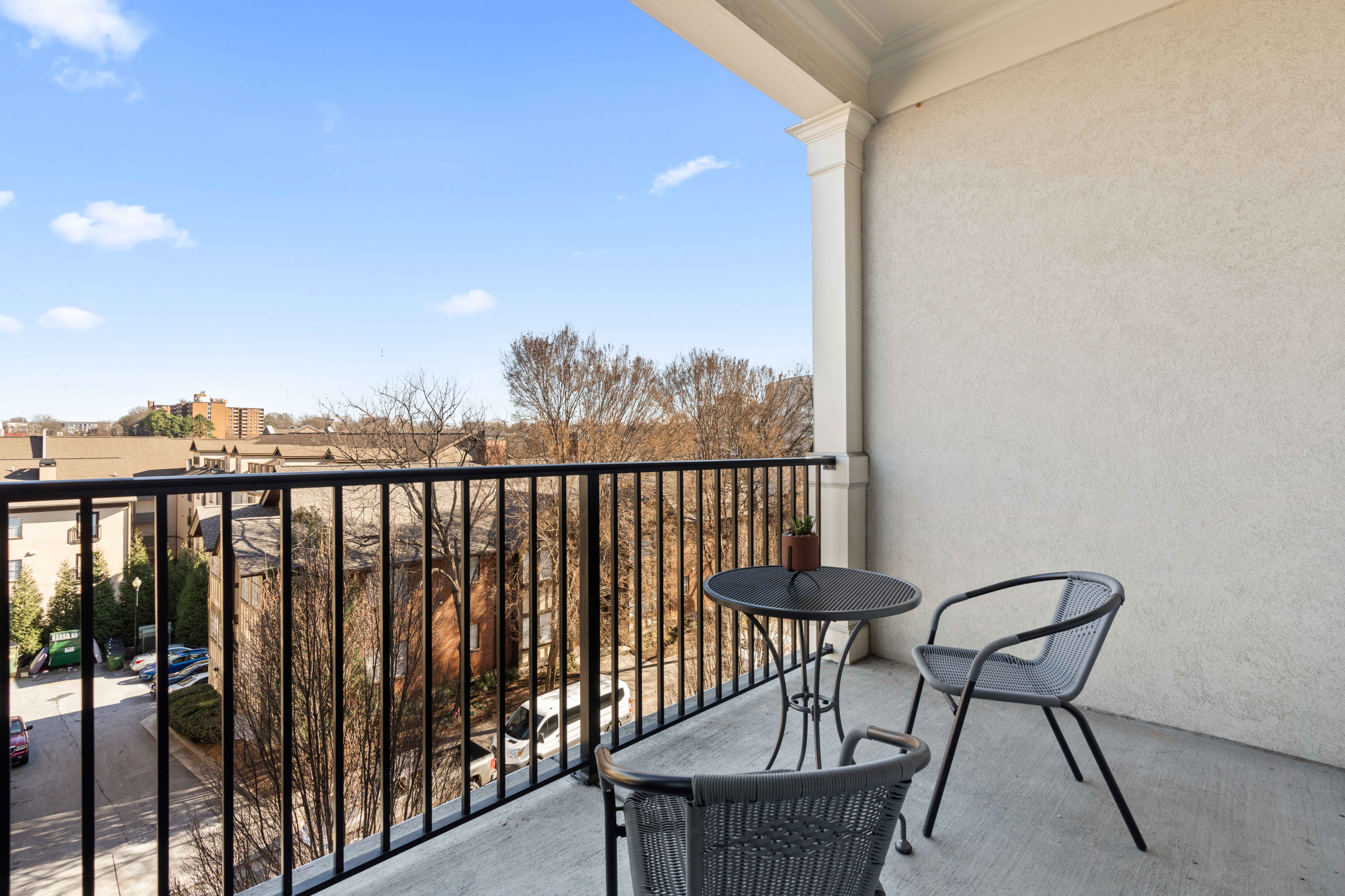 Charming balcony with cozy seating and table, offering a scenic view of a peaceful neighborhood under a clear blue sky.