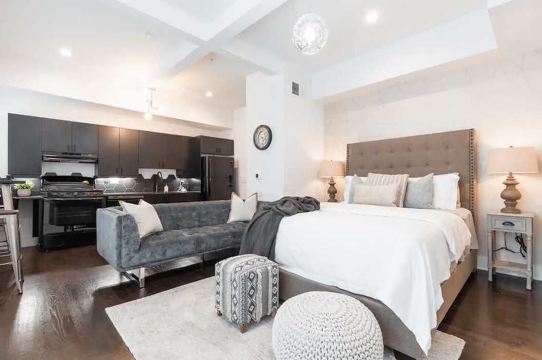 Chic studio apartment showcasing a cozy bedroom with stylish decor, open kitchen with dark cabinetry, and elegant lighting.