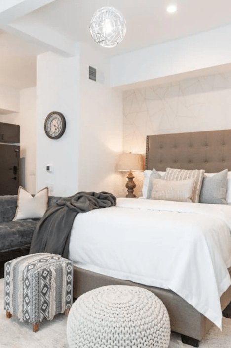 Cozy bedroom featuring a plush bed with elegant cushions, stylish ottoman, and soft lighting creating a warm ambiance.
