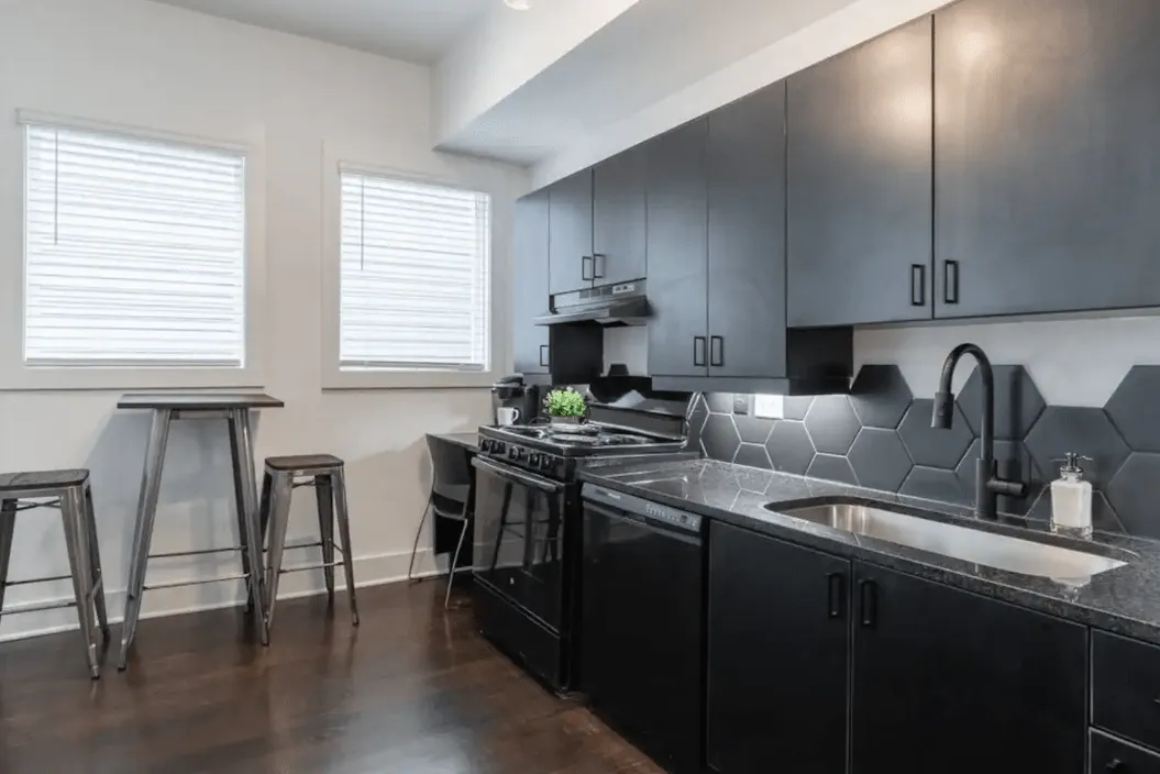 Modern kitchen with sleek black cabinets, a stylish hexagonal backsplash, and wooden bar seating, offering a chic and functional cooking space.