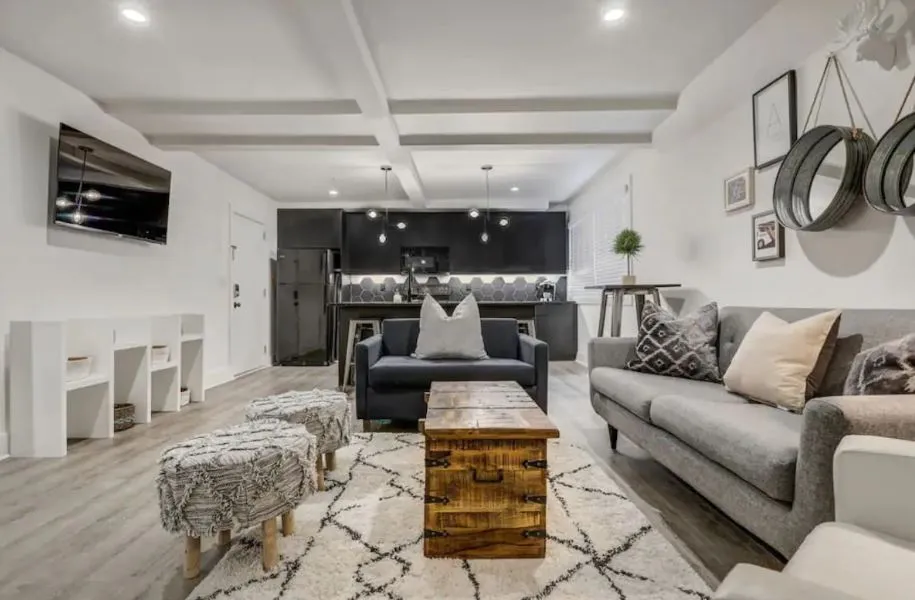 Inviting open-concept living area with modern decor, featuring a cozy gray sofa, chic kitchen with black cabinetry, and stylish pendant lighting.