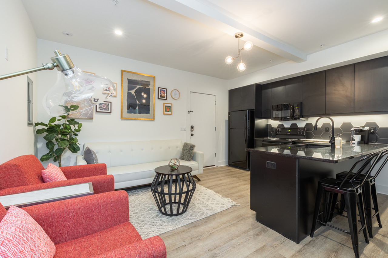 Chic living area with stylish red chairs, white sofa, and modern kitchen, featuring sleek black cabinetry and island.