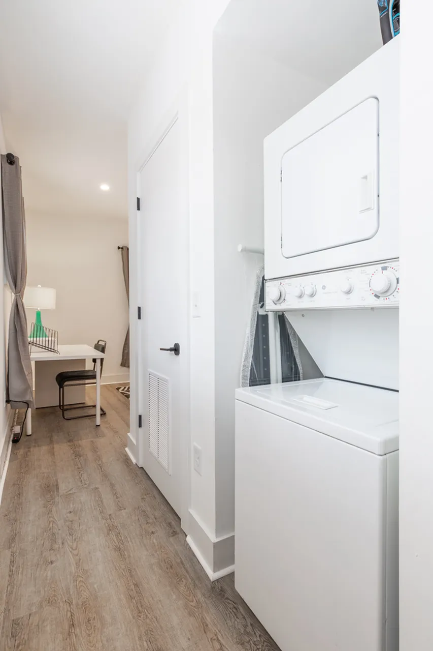 Modern apartment hallway with in-unit stacked washer and dryer, leading to a cozy workspace with a desk and chair.