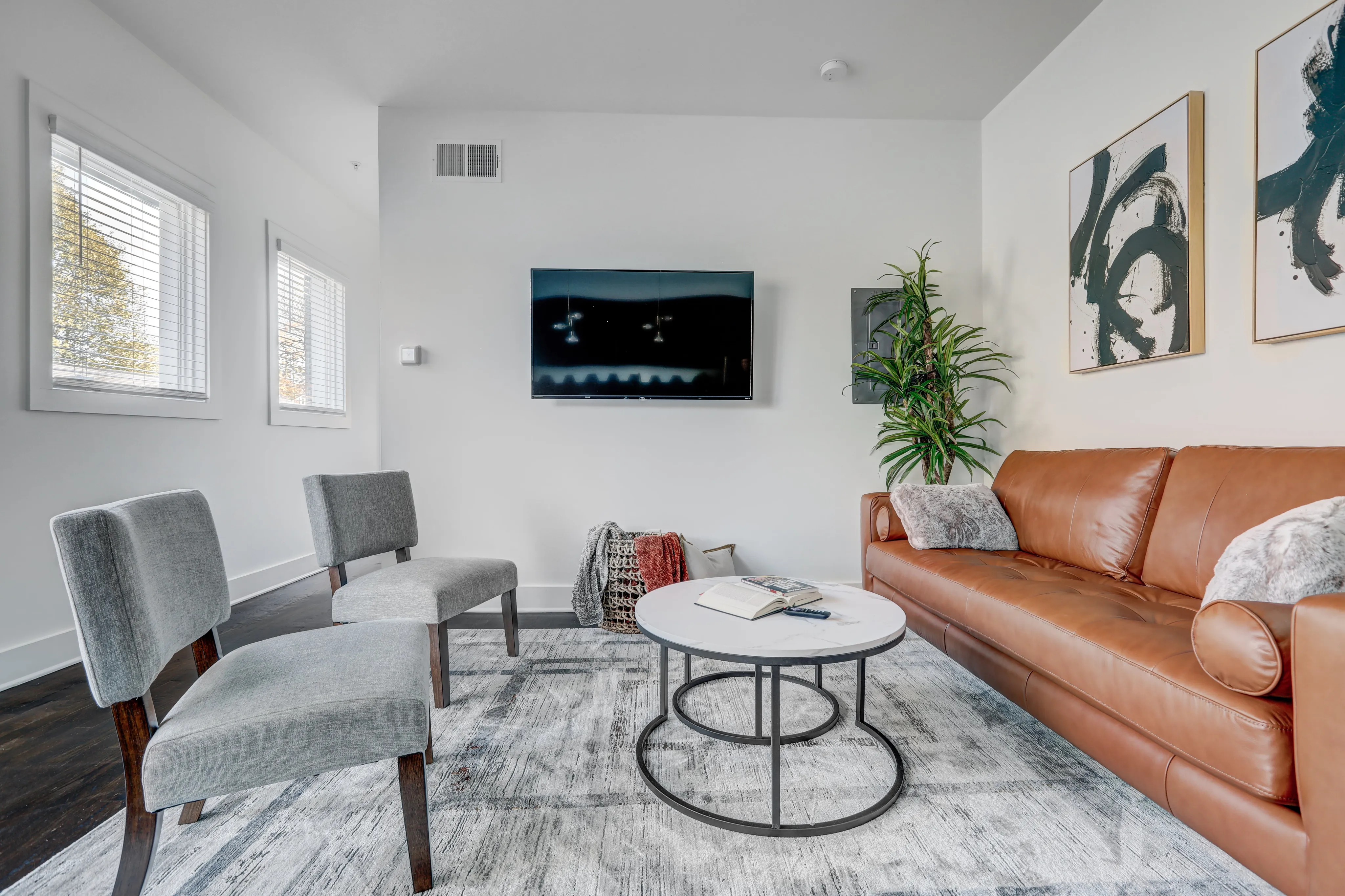 Modern living room with chic decor featuring a leather sofa, stylish armchairs, and a sleek coffee table, accented by contemporary artwork and lush greenery.