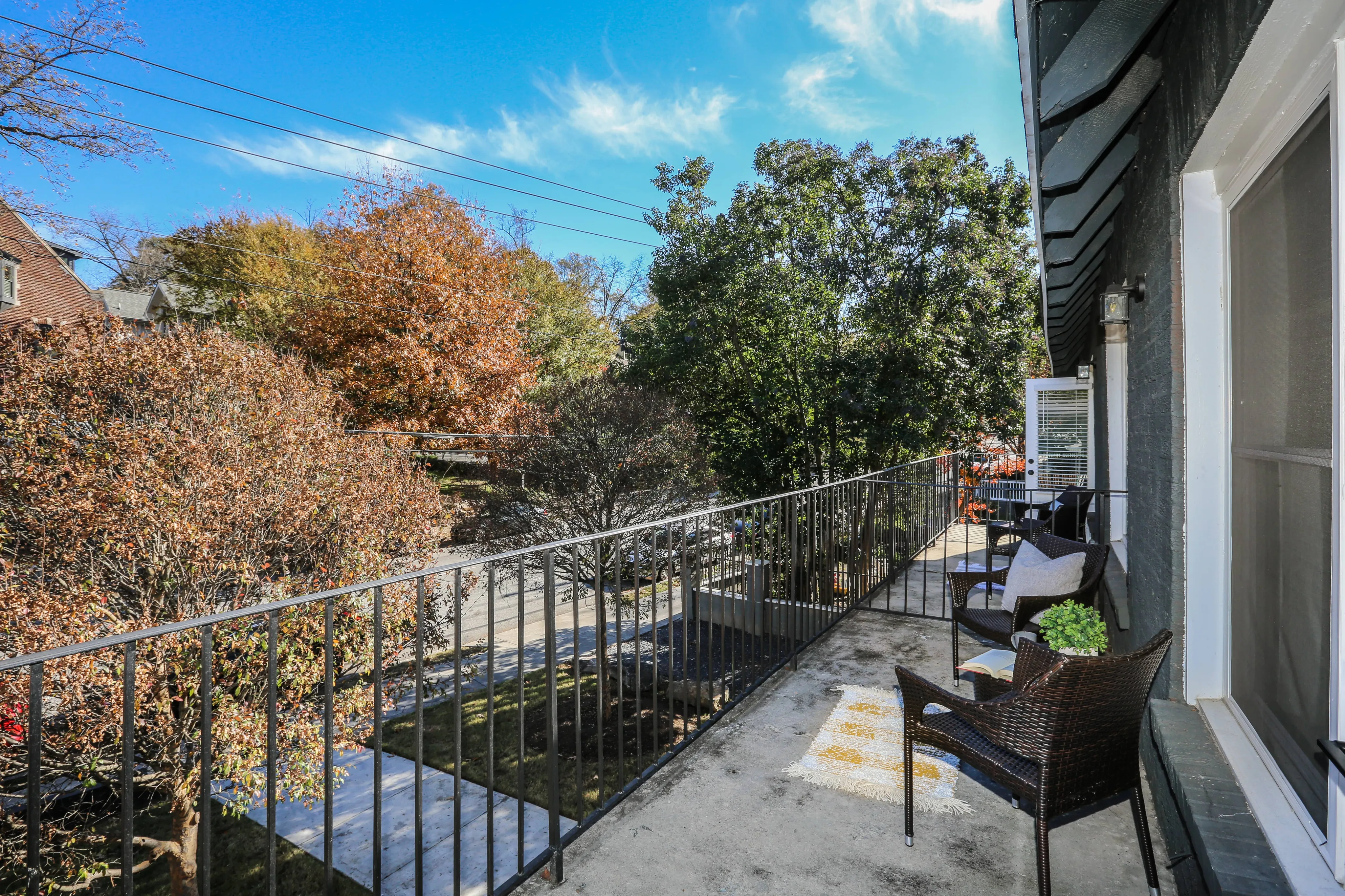 Charming balcony view featuring seating with lush green trees and clear blue sky, providing a serene outdoor retreat.