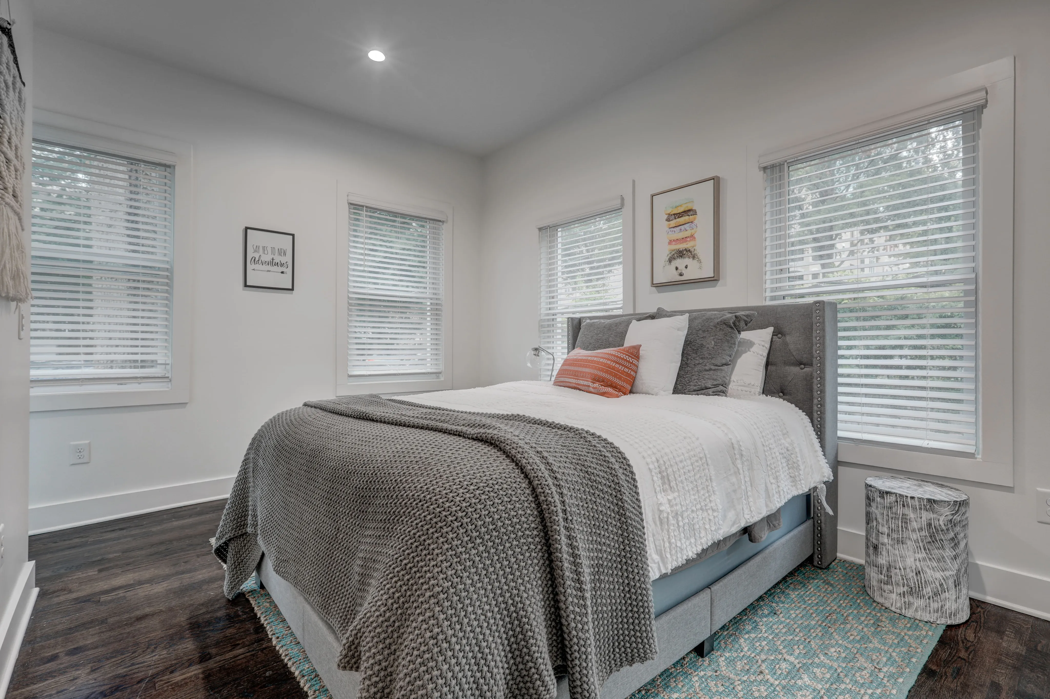 Bright and cozy bedroom with elegant decor, featuring a plush gray bed, soft textiles, and abundant natural light from multiple windows.