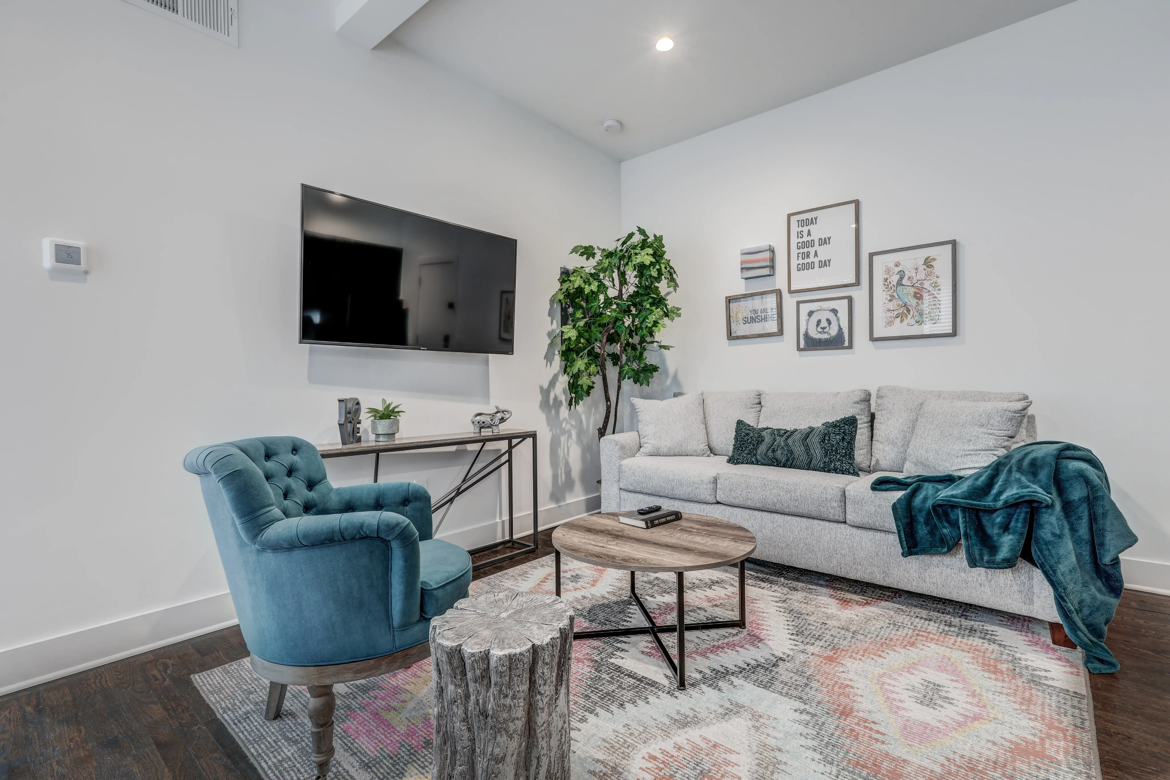 Chic living room featuring a plush gray sofa, vibrant teal armchair, wall-mounted TV, and stylish decor accents on a patterned rug.