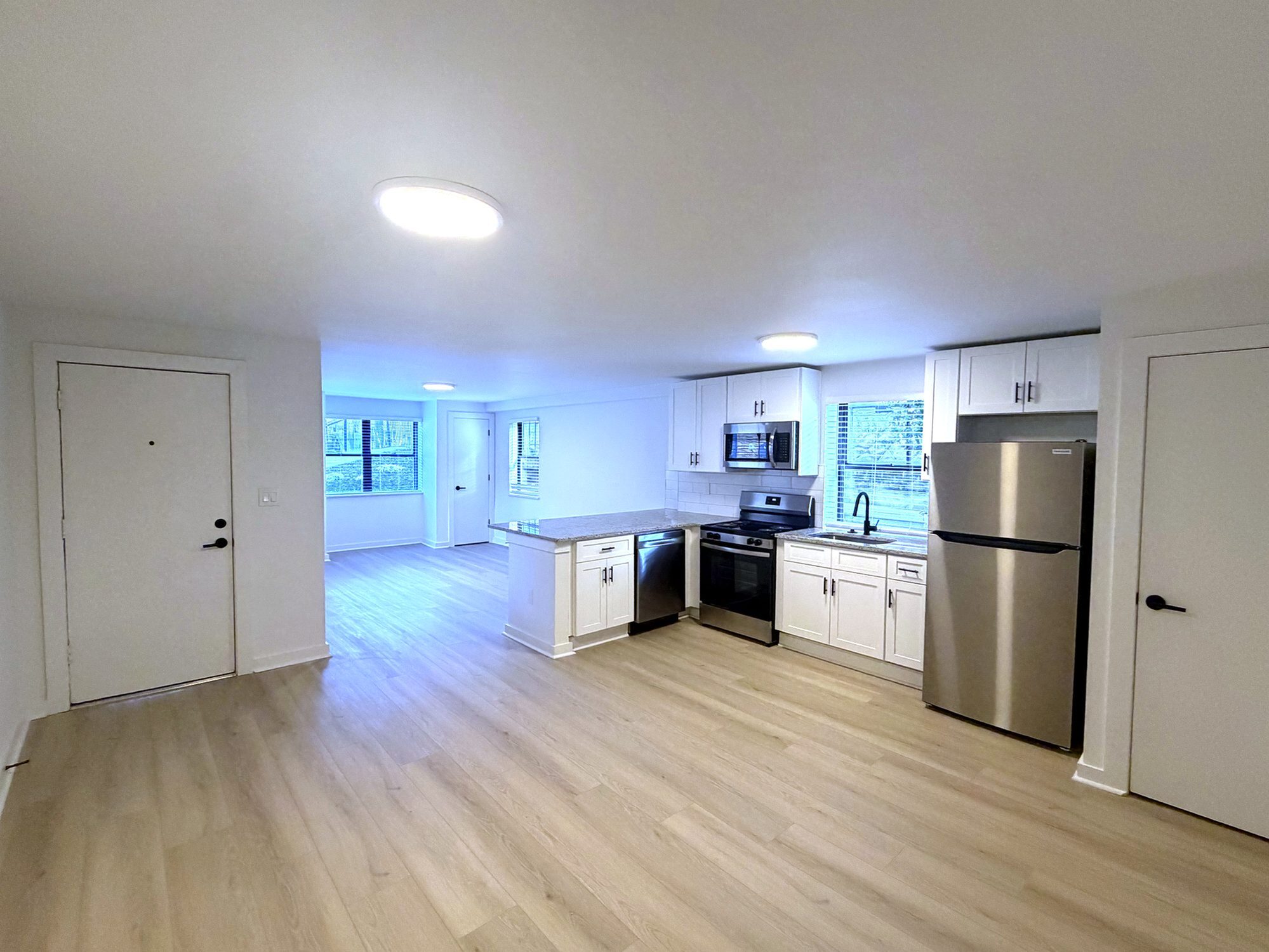 Bright, modern kitchen with stainless steel appliances, sleek white cabinets, and spacious open layout with new floors.