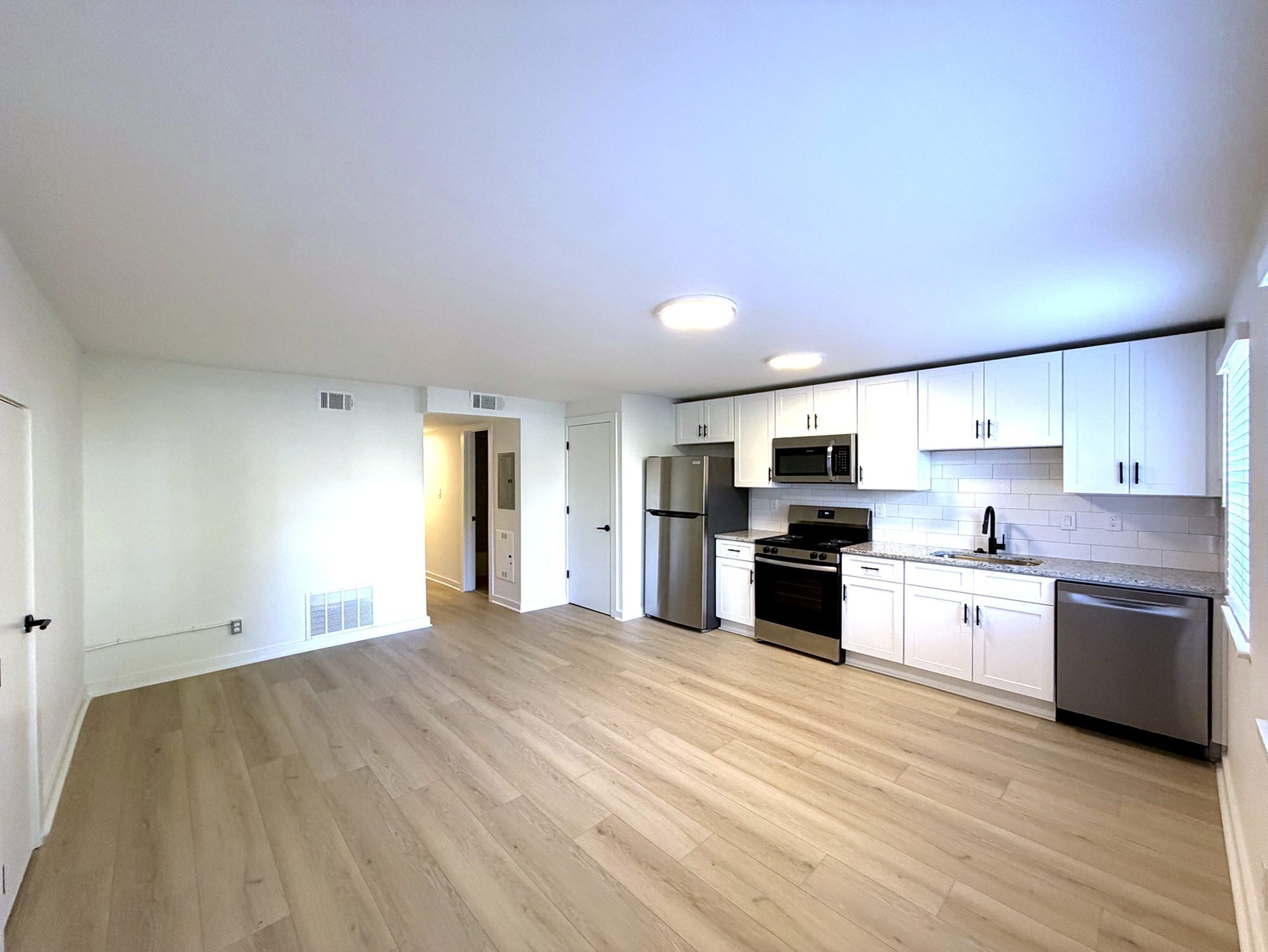 Bright, modern kitchen with stainless steel appliances, sleek white cabinetry, and elegant wood flooring, offering a spacious and welcoming environment.