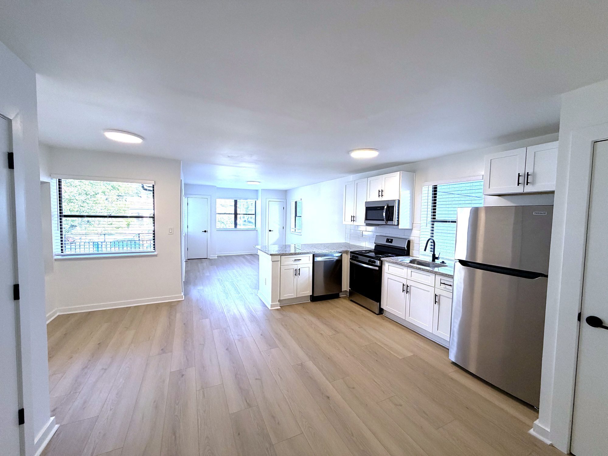 Bright, open-concept kitchen and living area with sleek stainless steel appliances and modern white cabinetry.