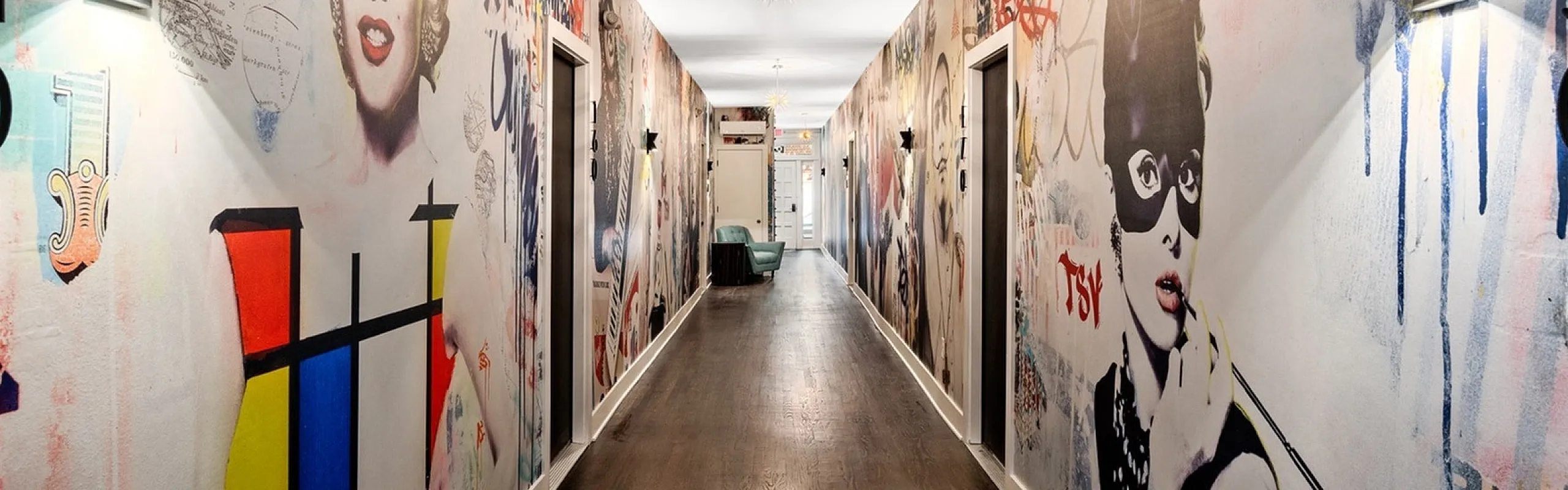 Vibrant hallway adorned with eclectic pop art murals, featuring polished wood flooring and elegant wall sconces, creating a modern and artistic ambiance.