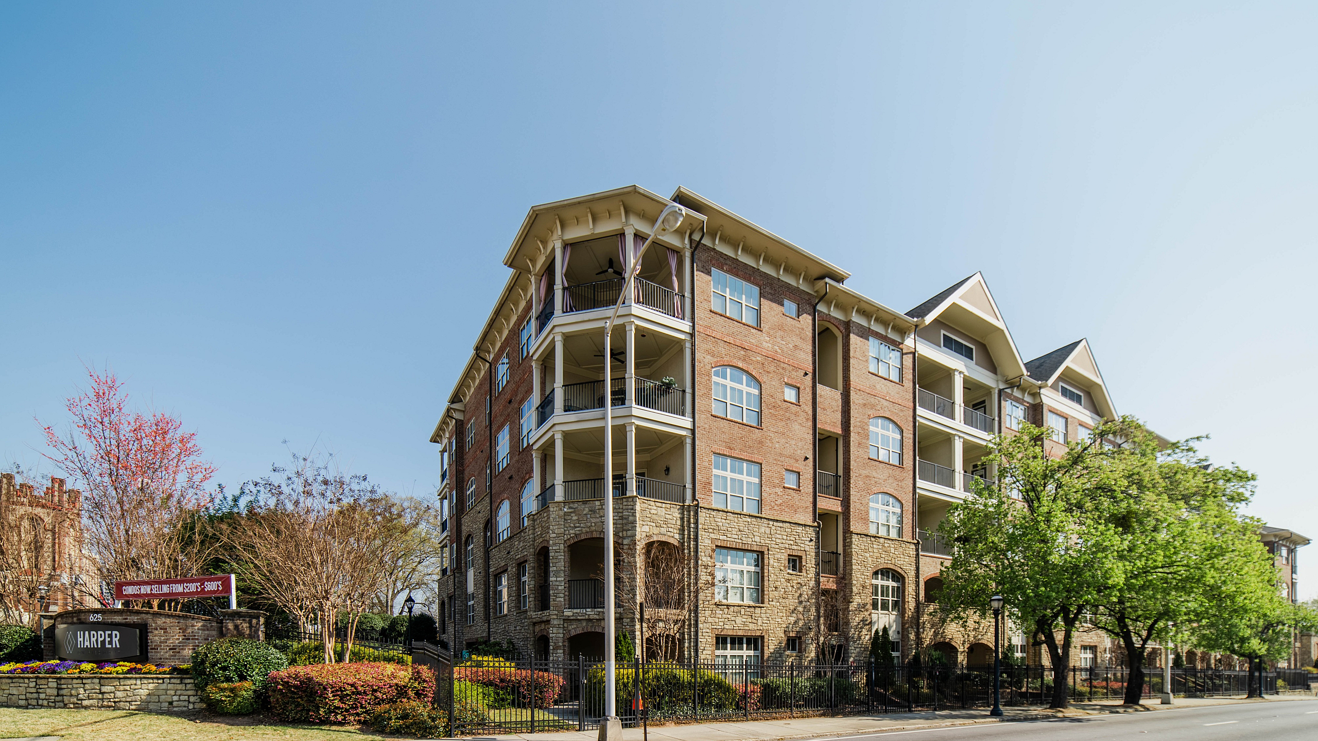 Charming brick apartment building with spacious balconies, nestled on a tree-lined street in a vibrant neighborhood.